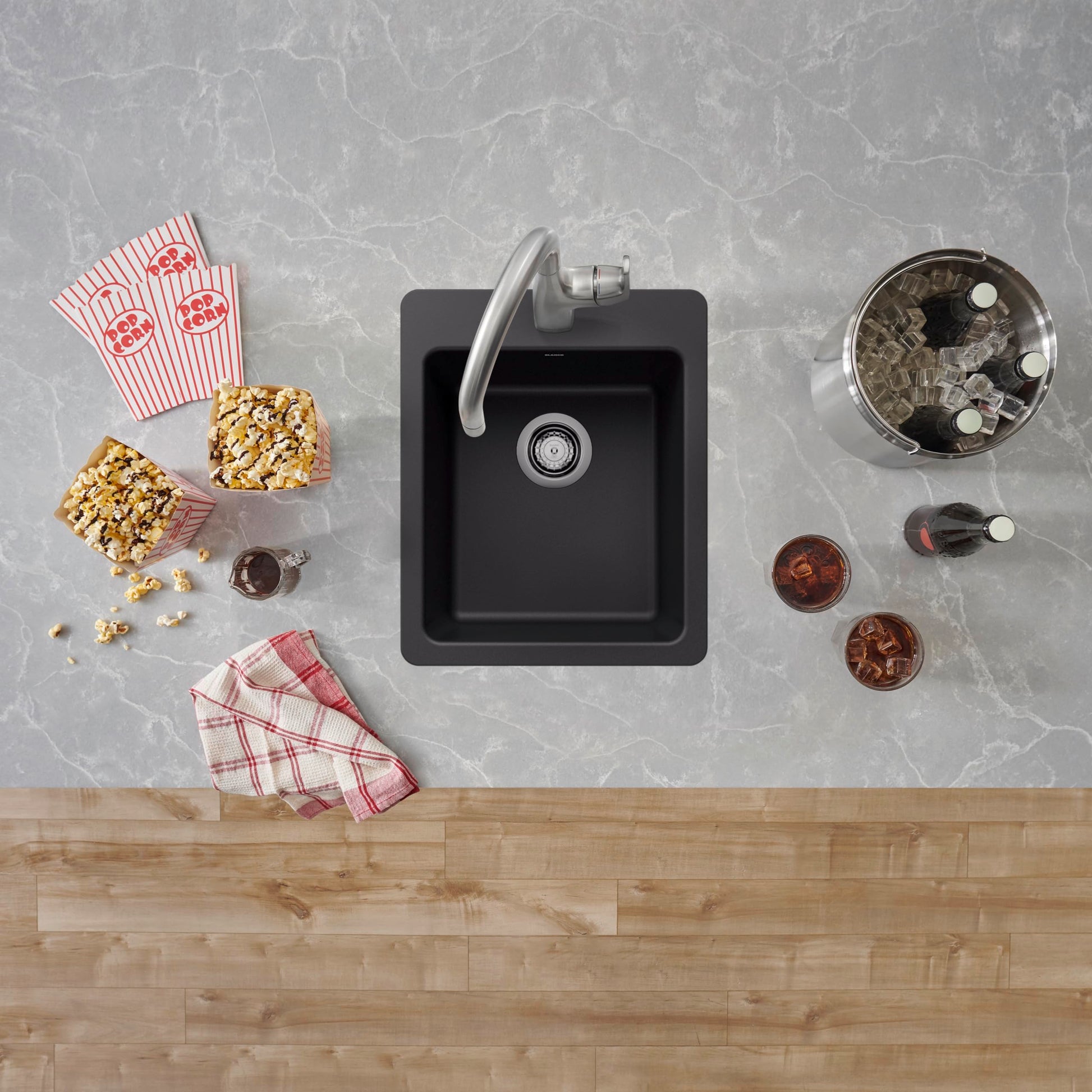 Coal black square bar sink with single basin and faucet mounted on gray marble countertop next to wood cabinet.