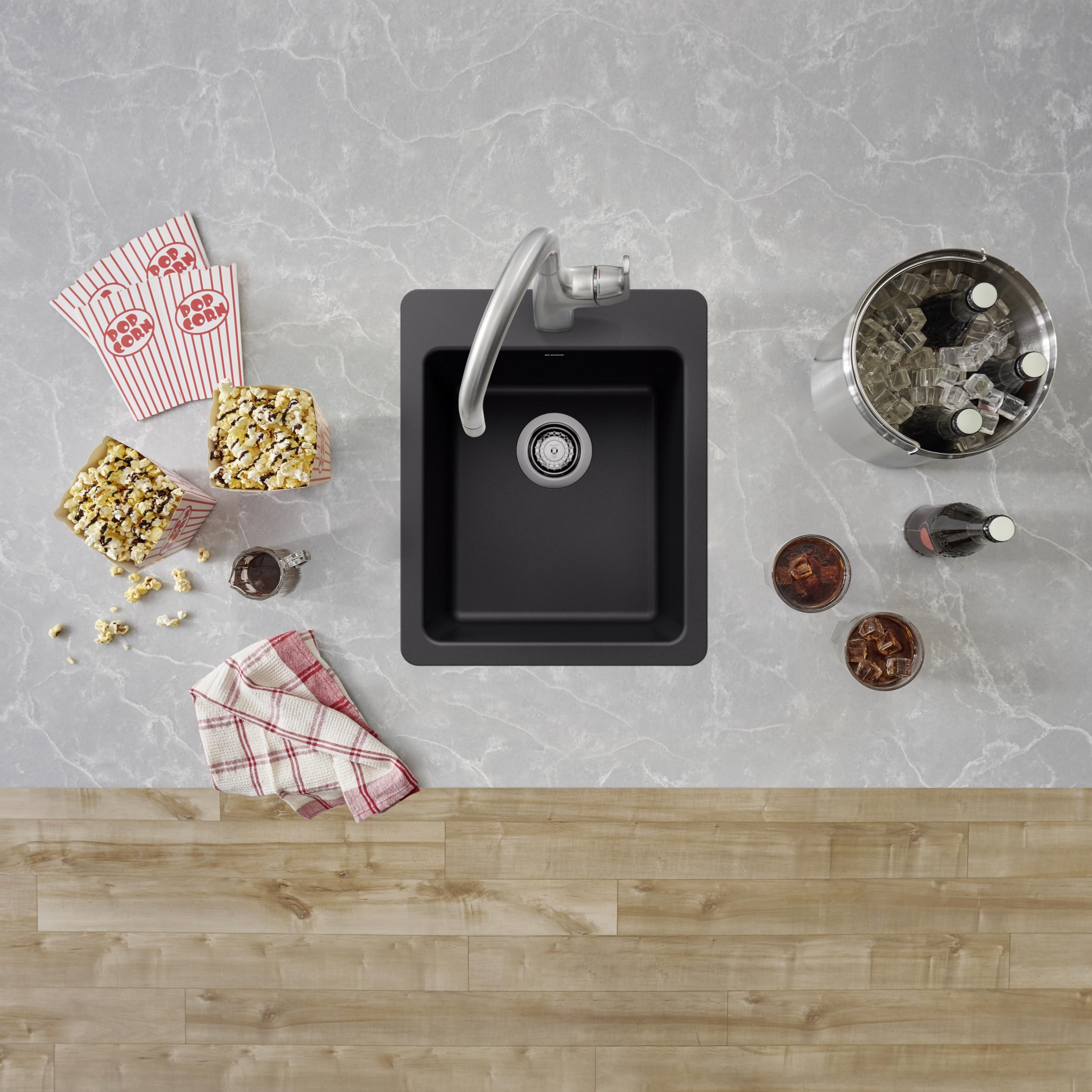 Coal black square bar sink with single basin and faucet mounted on gray marble countertop next to wood cabinet.
