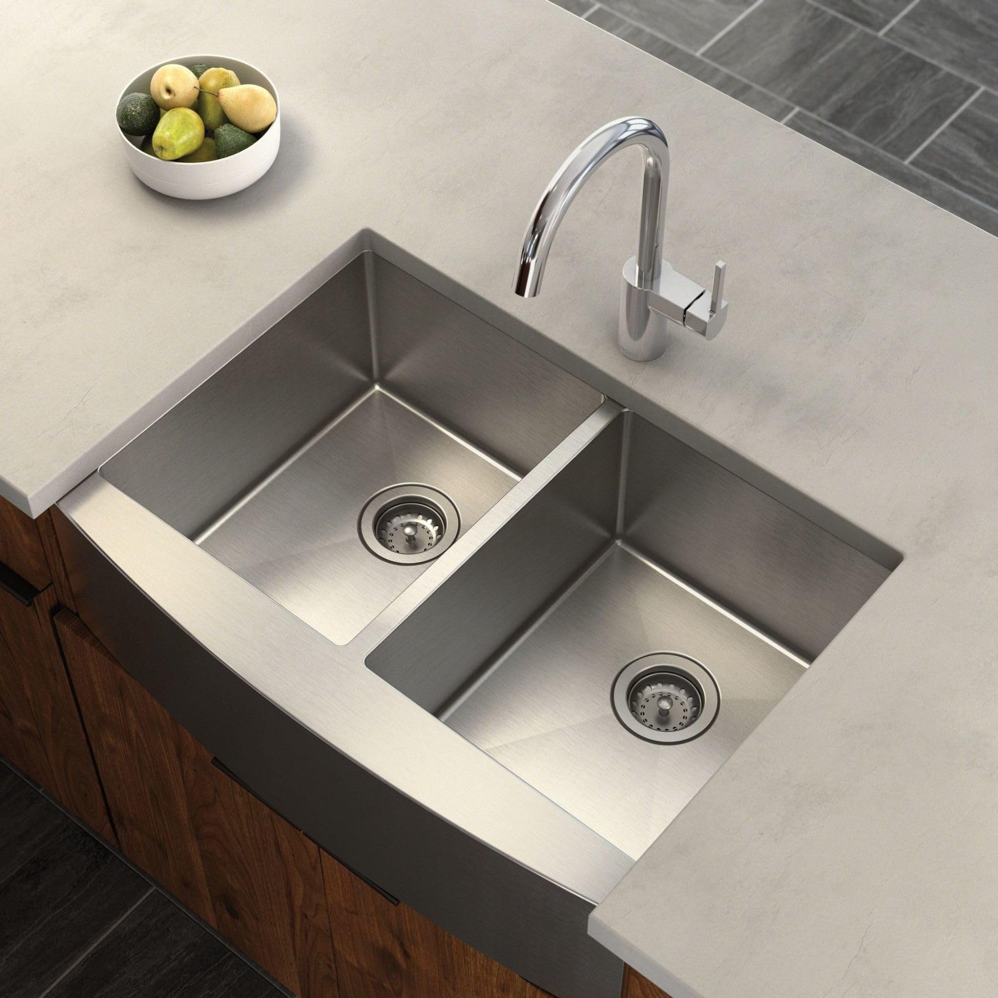 Stainless steel double bowl farmhouse sink with apron front and two drain strainers installed in countertop.