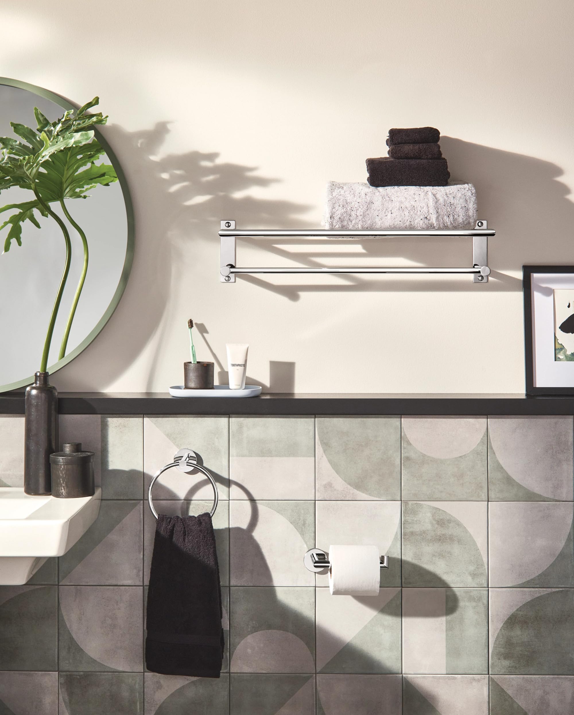 Chrome single-post toilet paper holder mounted on tiled bathroom wall below towel shelf.