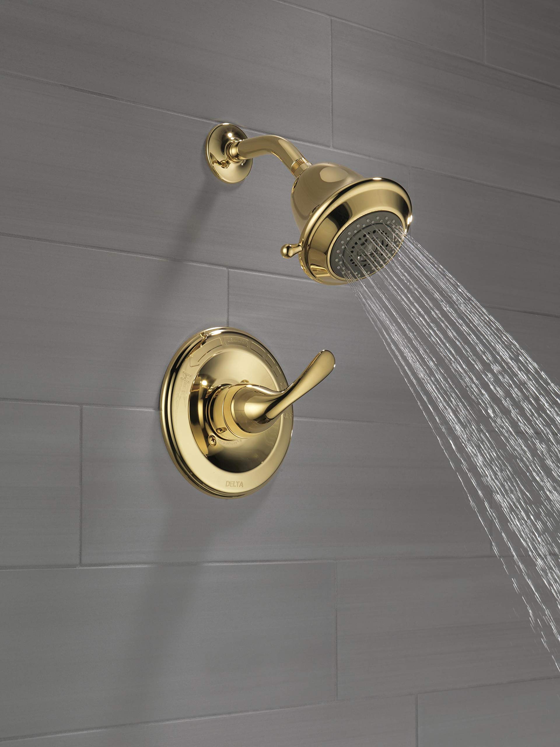 Polished brass shower trim with single lever handle, round wall-mounted valve, and matching showerhead with water stream on g