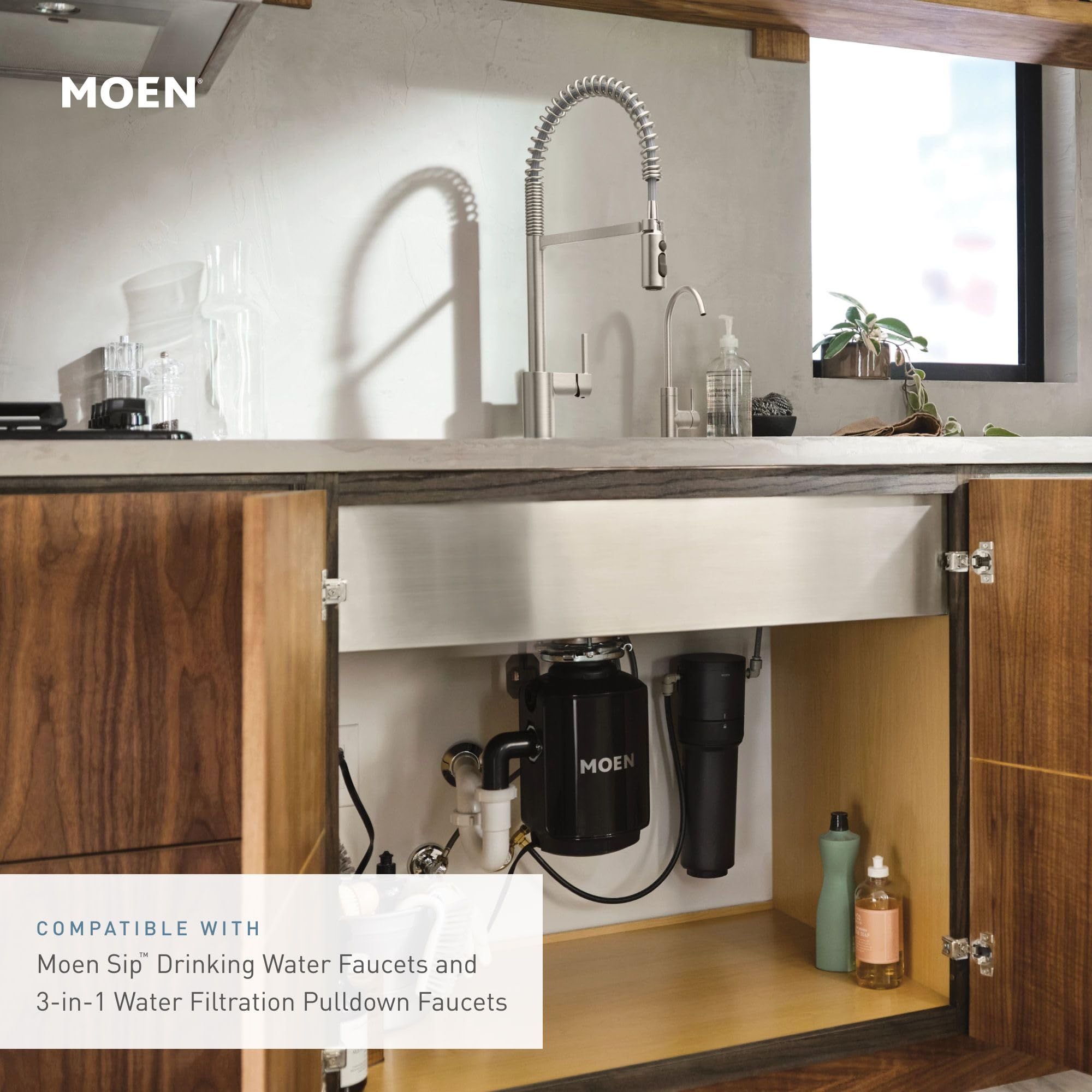 Chrome under-sink water filtration system with black cylindrical filter cartridges installed beneath a farmhouse sink.
