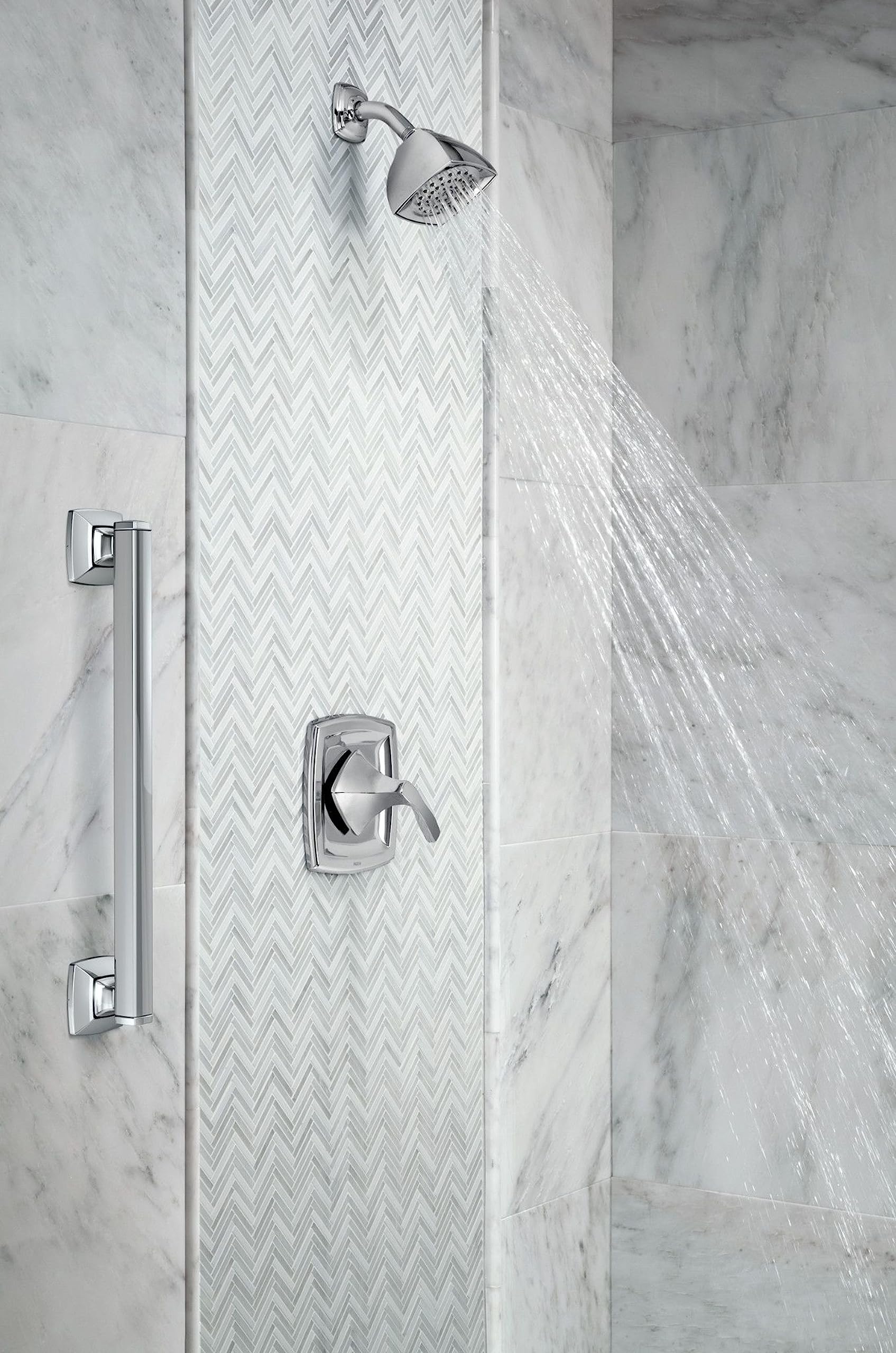 Chrome tub and shower trim kit with single-handle valve, shower head, and hand shower mounted on marble tile wall.