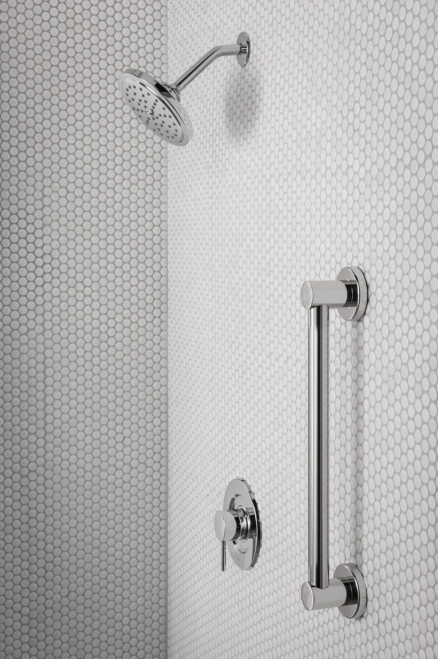 Chrome shower valve trim with curved arm, round showerhead, vertical grab bar, and dual control handles mounted on tile wall.