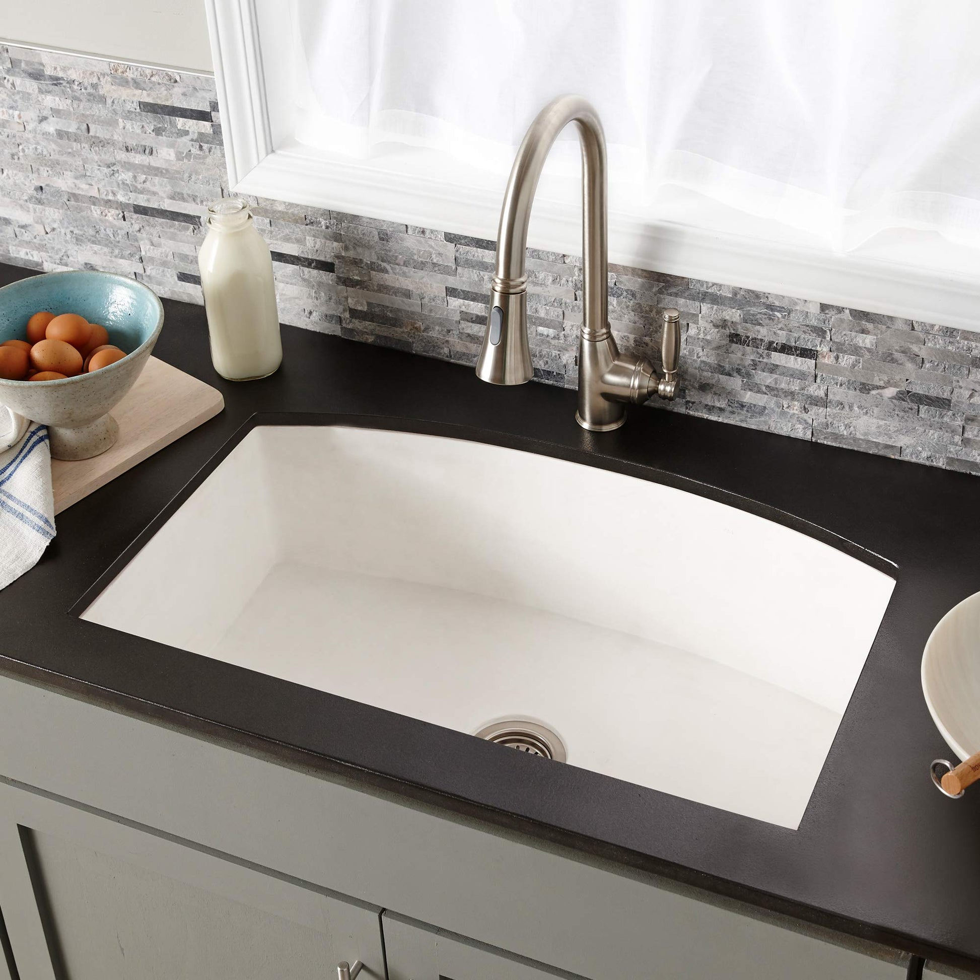 Pearl white farmhouse kitchen sink with single rectangular basin and brushed nickel faucet installed in black countertop.
