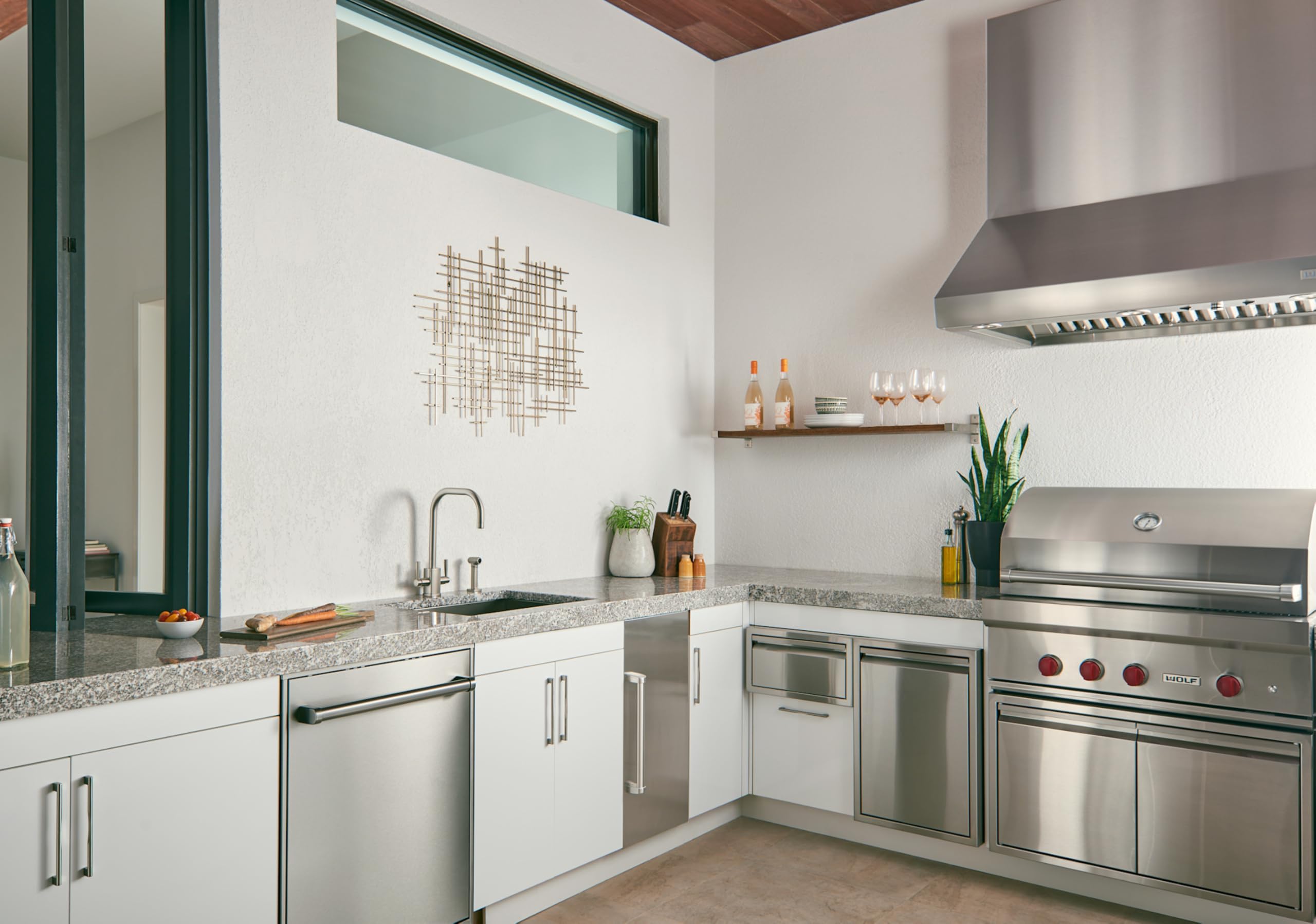 Brushed stainless steel single bowl sink installed in modern kitchen with white cabinetry and granite countertop.