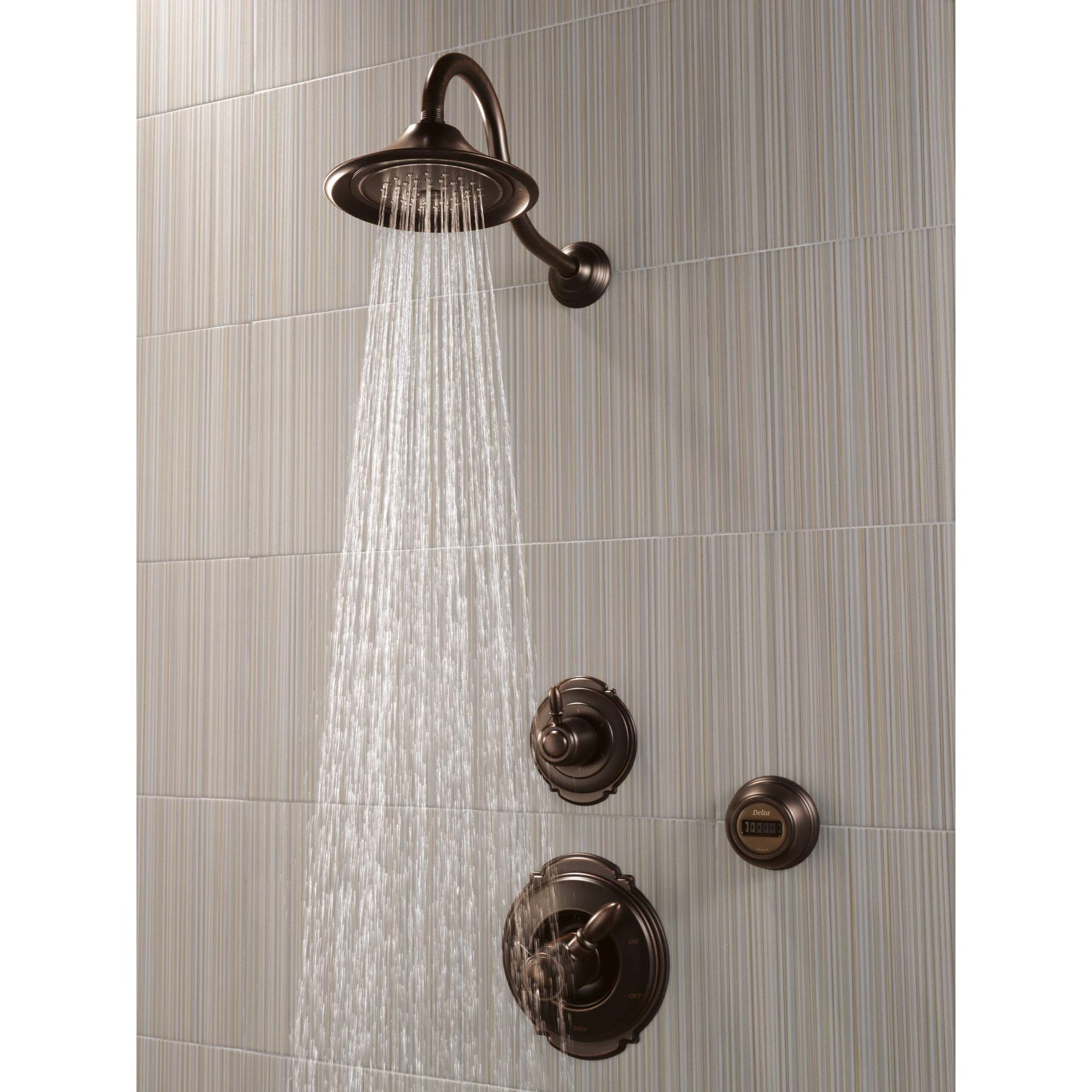 Venetian bronze shower head with curved arm mounted on tile wall, water flowing from round head and control knobs below.