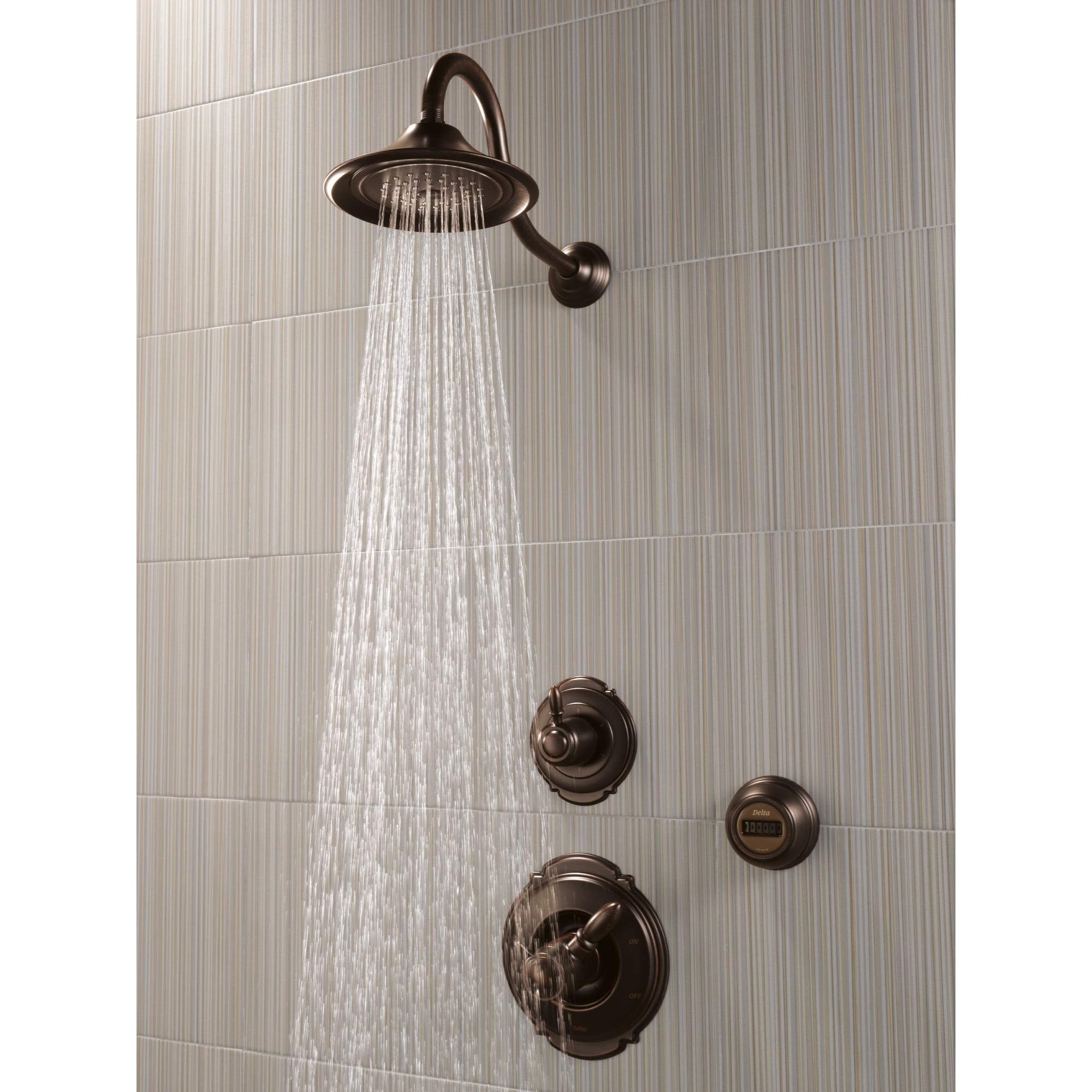 Venetian bronze shower head with curved arm mounted on tile wall, water flowing from round head and control knobs below.