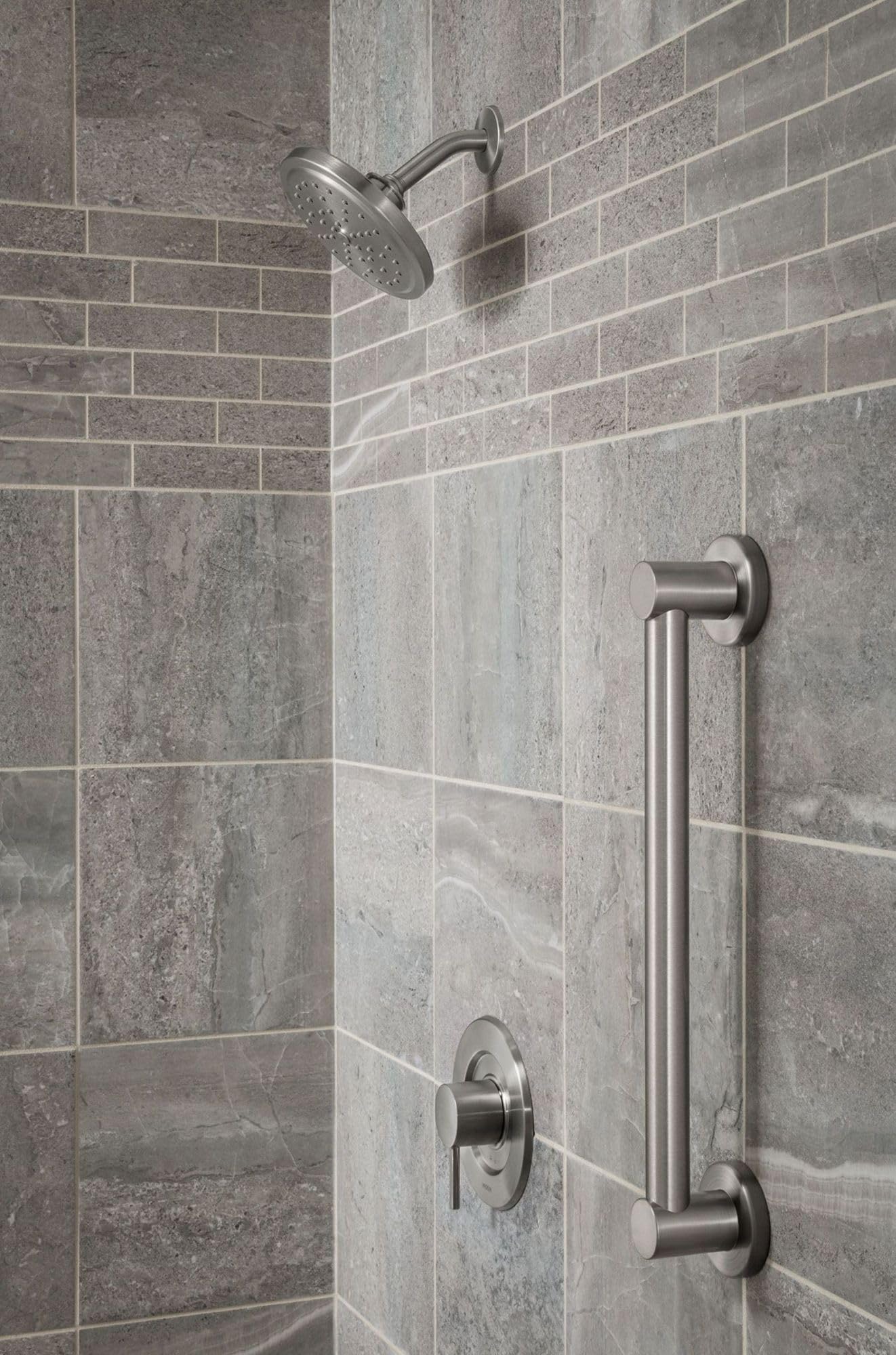Brushed nickel grab bar mounted vertically on tiled shower wall next to showerhead and control valve.