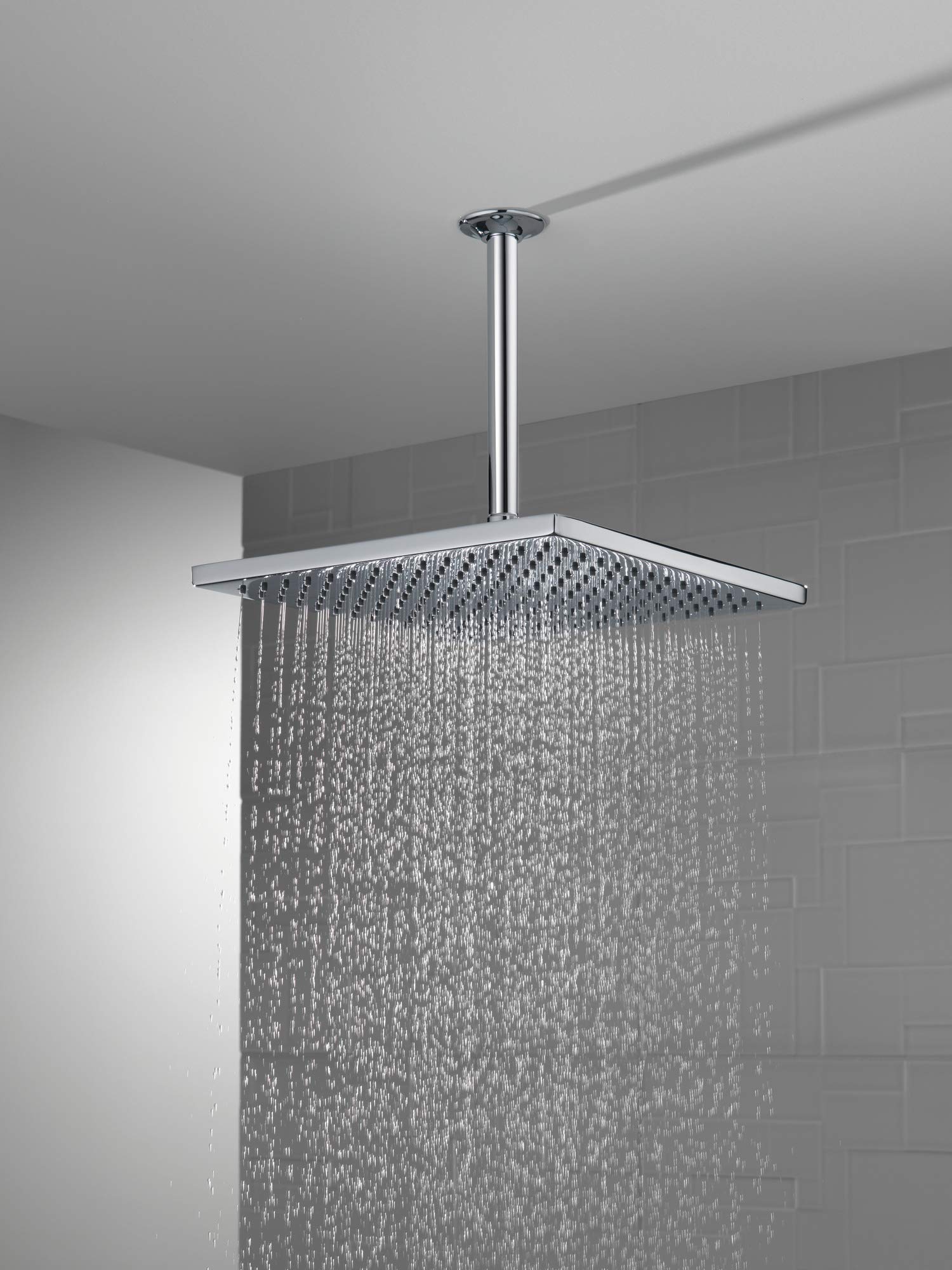 Chrome raincan shower head mounted to ceiling with vertical arm, dispensing water from perforated square panel.