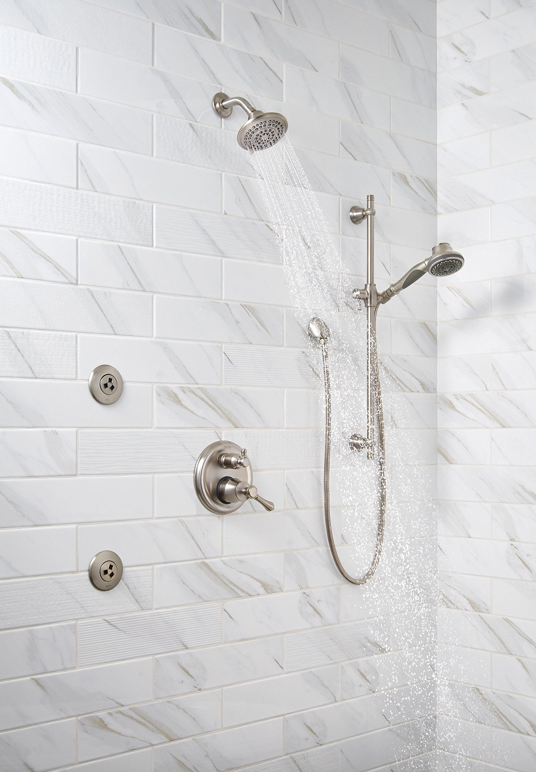 Stainless steel shower system with fixed overhead head, handheld wand, control valve, and body jets mounted on white tile wal