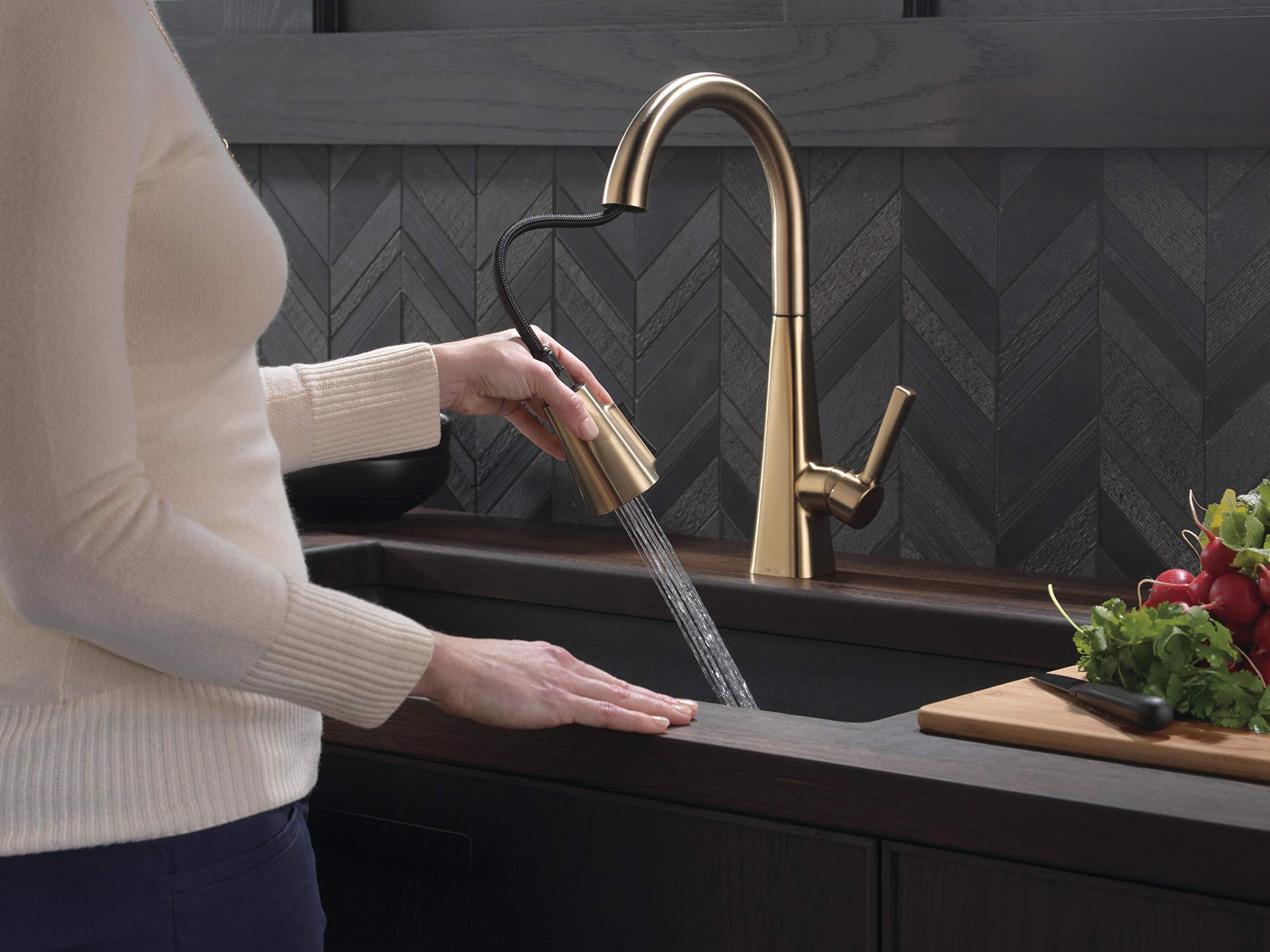 Champagne bronze single-handle pull-down kitchen faucet with curved spout over black sink and herringbone tile backsplash.