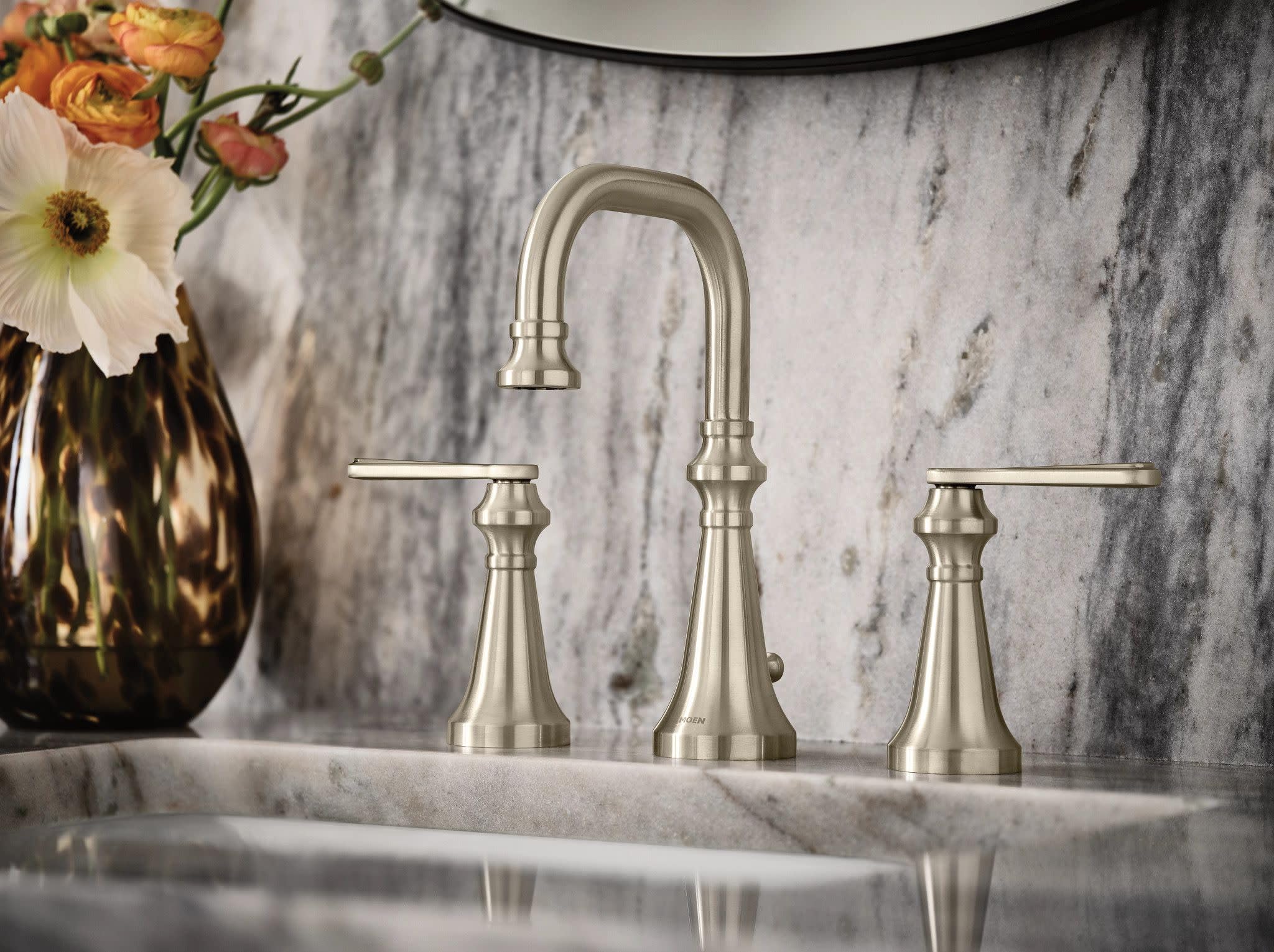 Brushed nickel two-handle bathroom faucet with high arc spout and lever handles on marble sink.