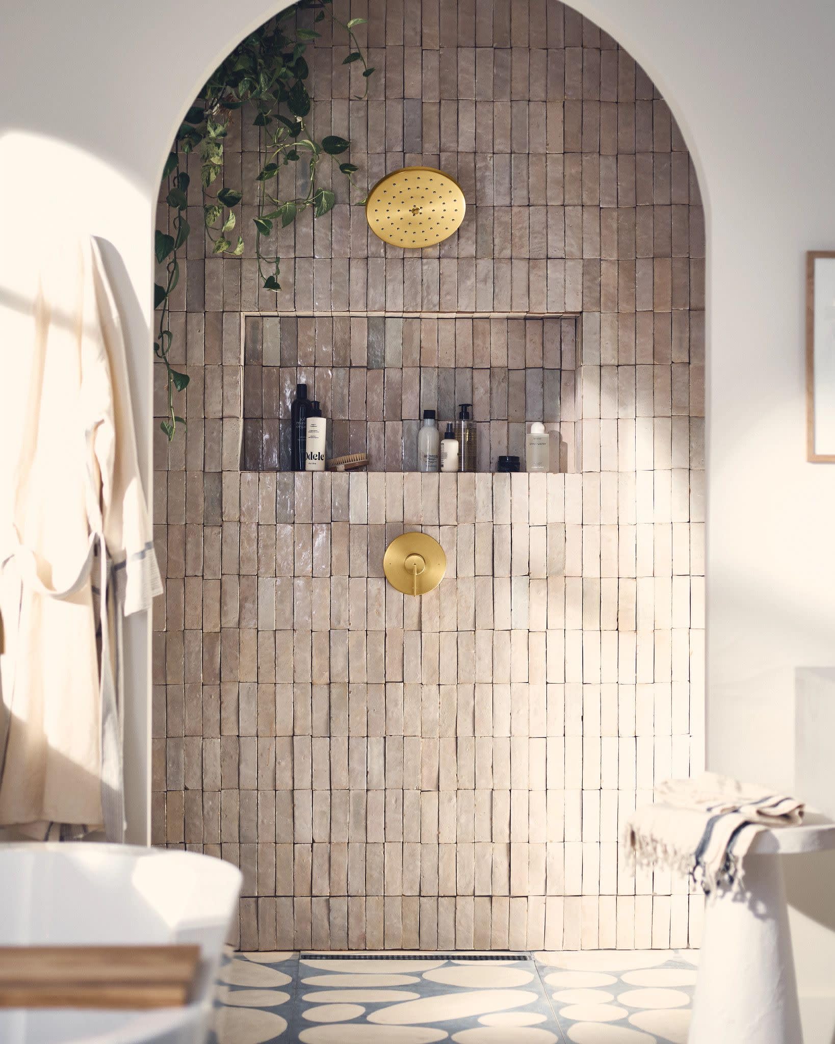 Brushed gold circular showerhead and single-handle trim mounted on tiled shower wall.