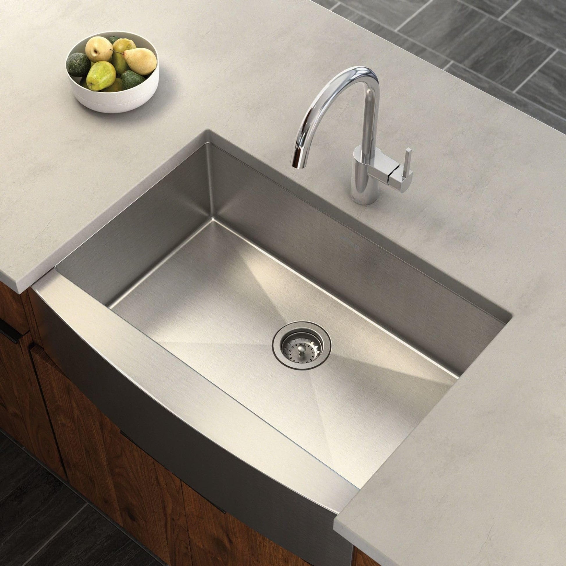 Stainless steel undermount farmhouse sink with apron front, single bowl, and chrome faucet installed in countertop.