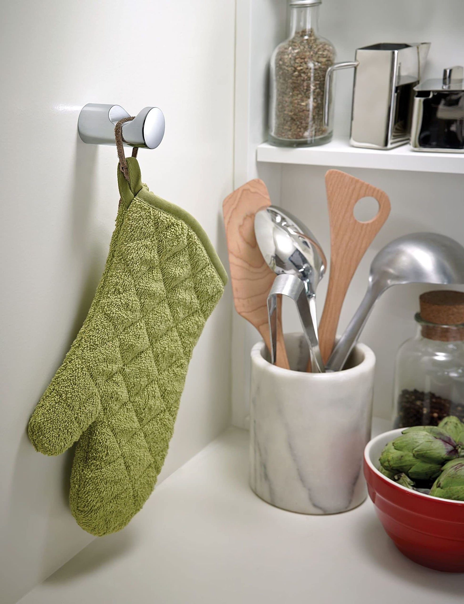 Chrome cylindrical robe hook mounted on white wall with green towel hanging from it.