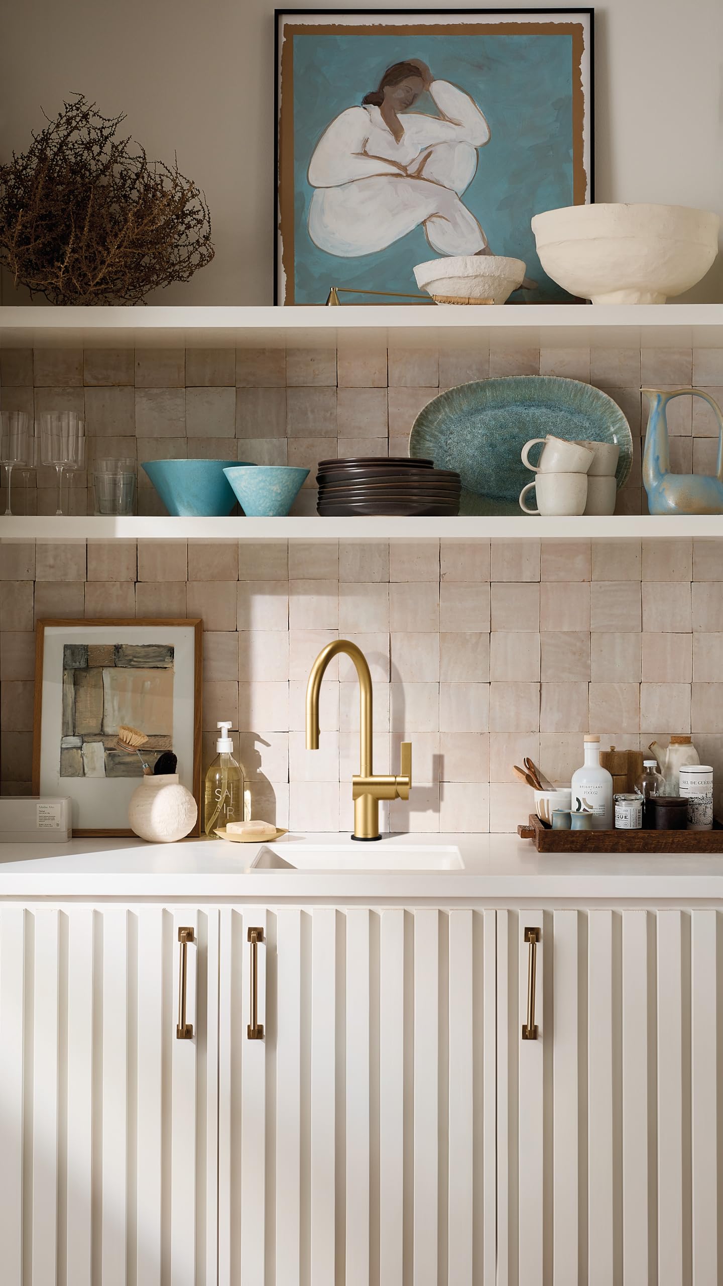 Brushed gold pulldown kitchen faucet with curved spout mounted above white sink in tiled bathroom.