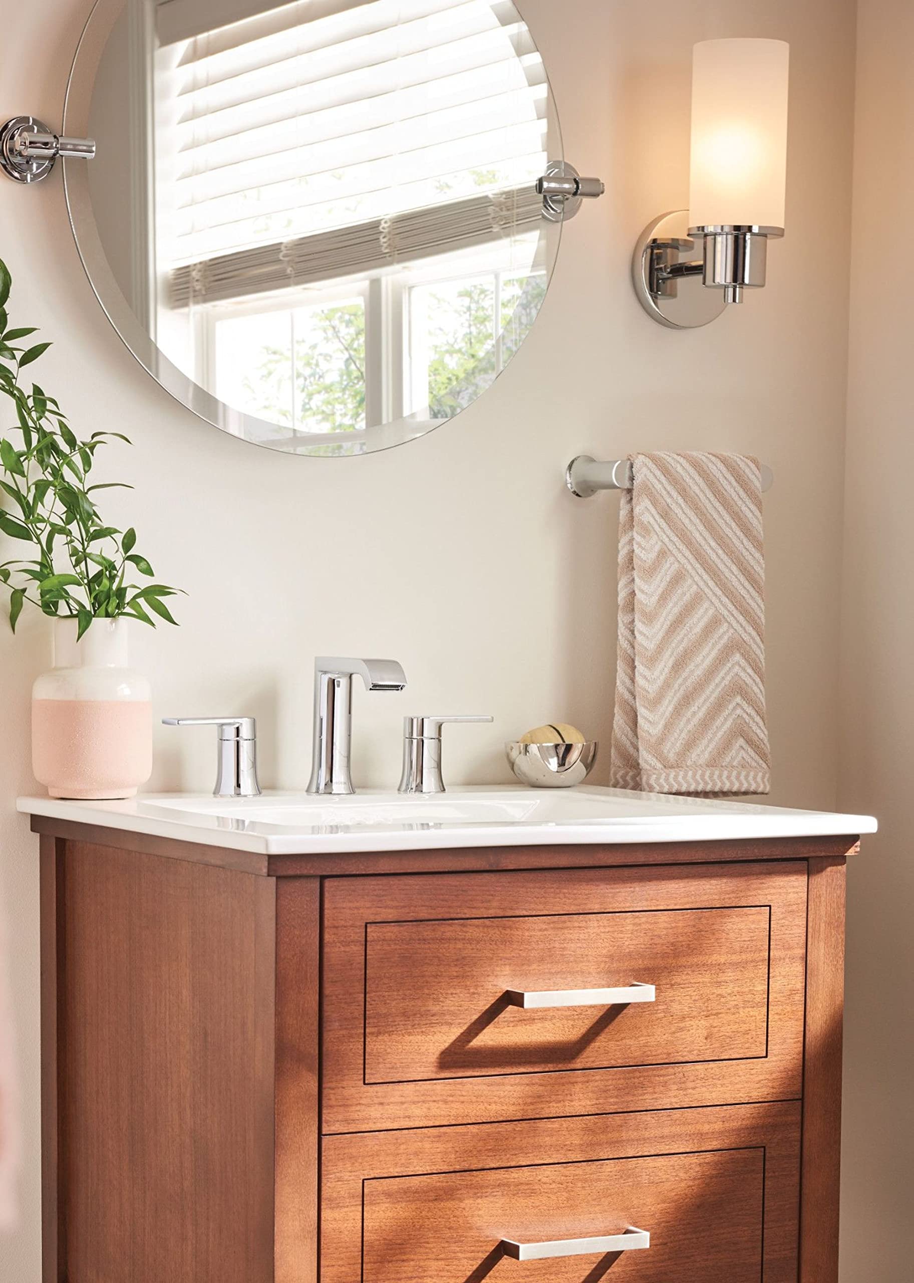 Chrome hand towel bar mounted on bathroom wall below mirror holding striped towel.