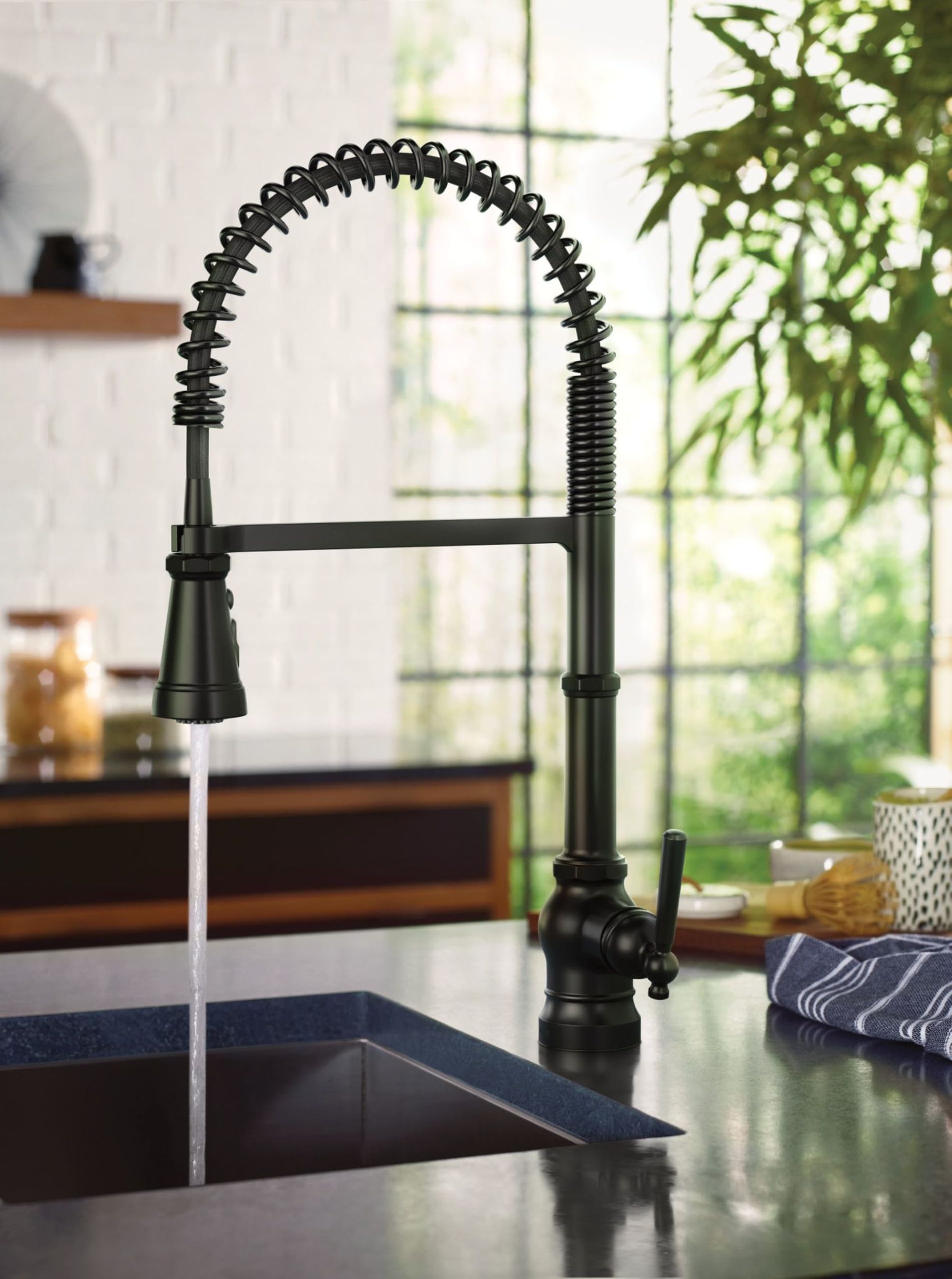 Matte black pulldown kitchen faucet with coiled hose and single handle over dark countertop sink.