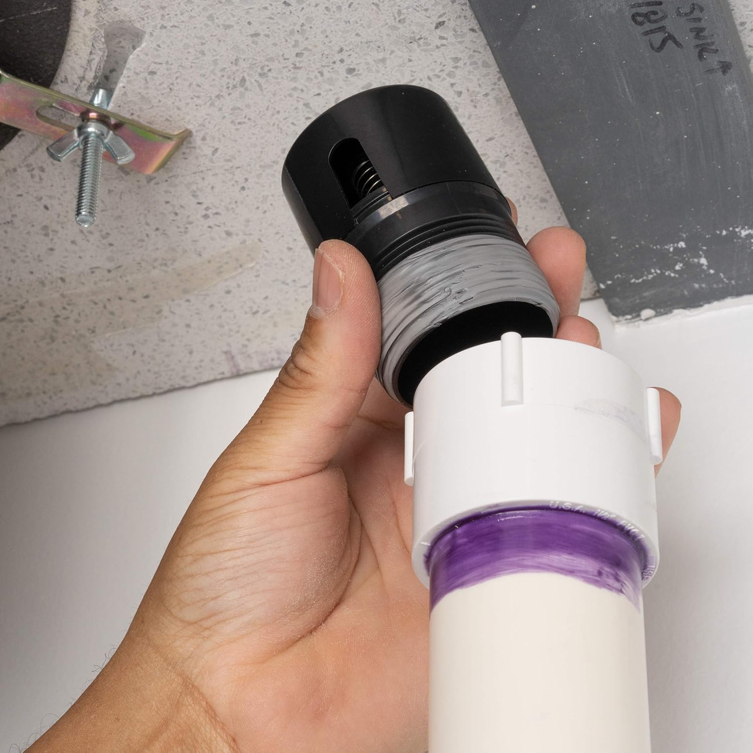Black and white ABS inline vent with purple seal band held in hand, showing threaded connection and internal valve.