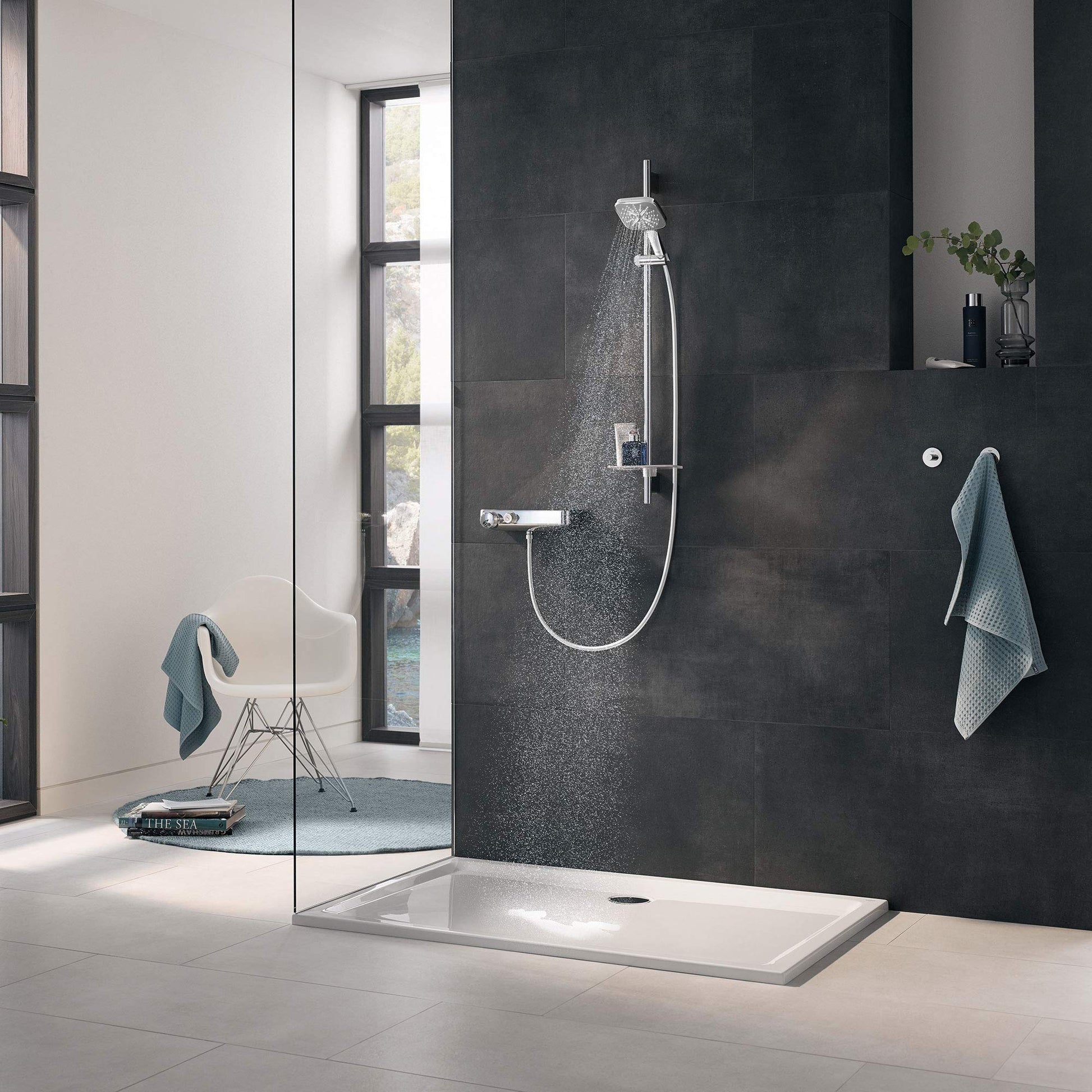 Chrome shower slide bar with handheld showerhead and hose mounted on dark tile wall above white shower base.