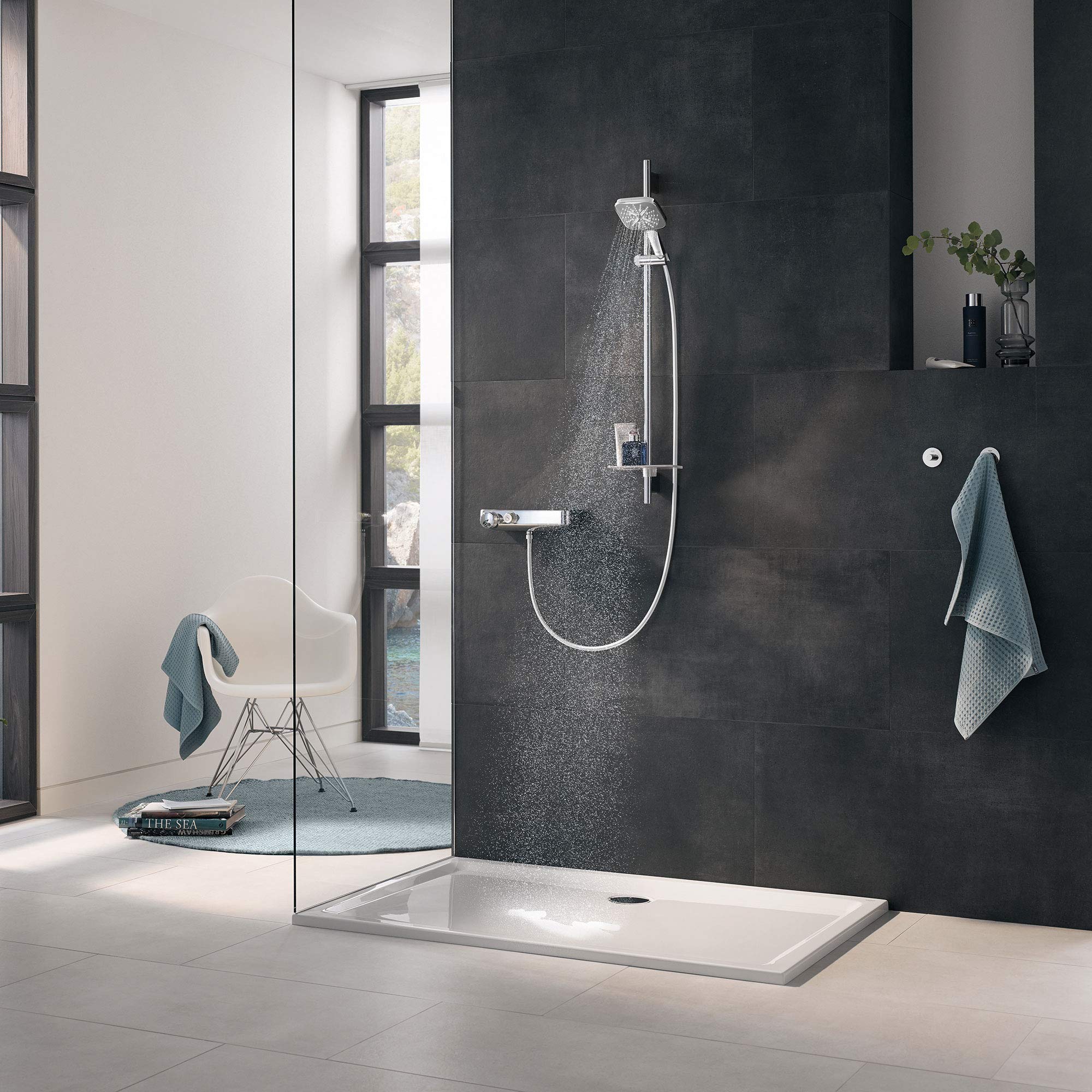 Chrome shower slide bar with handheld showerhead and hose mounted on dark tile wall above white shower base.