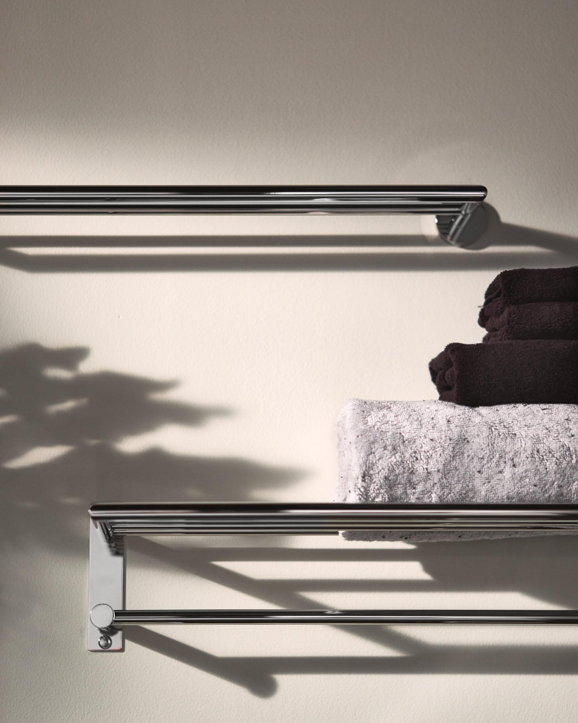 Chrome towel shelf with upper and lower bars holding rolled towels against white wall.