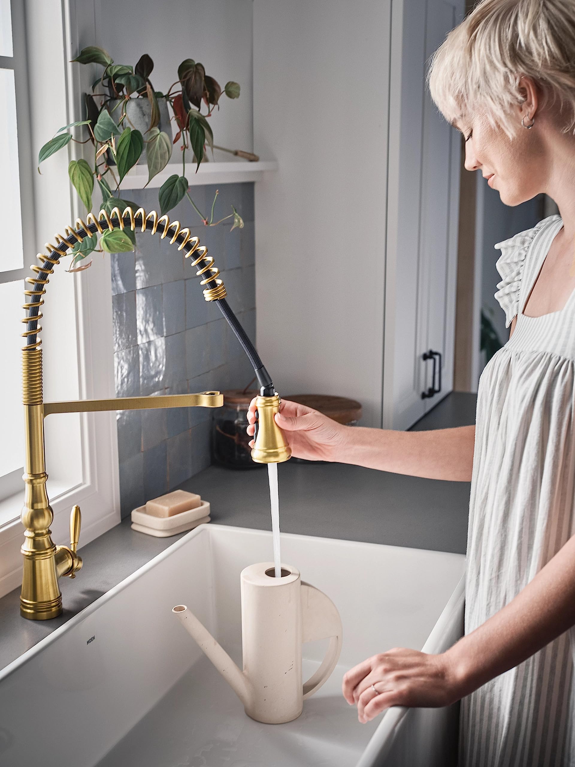 Brushed gold pulldown kitchen faucet with coiled hose and single handle, installed above white sink with water running into c
