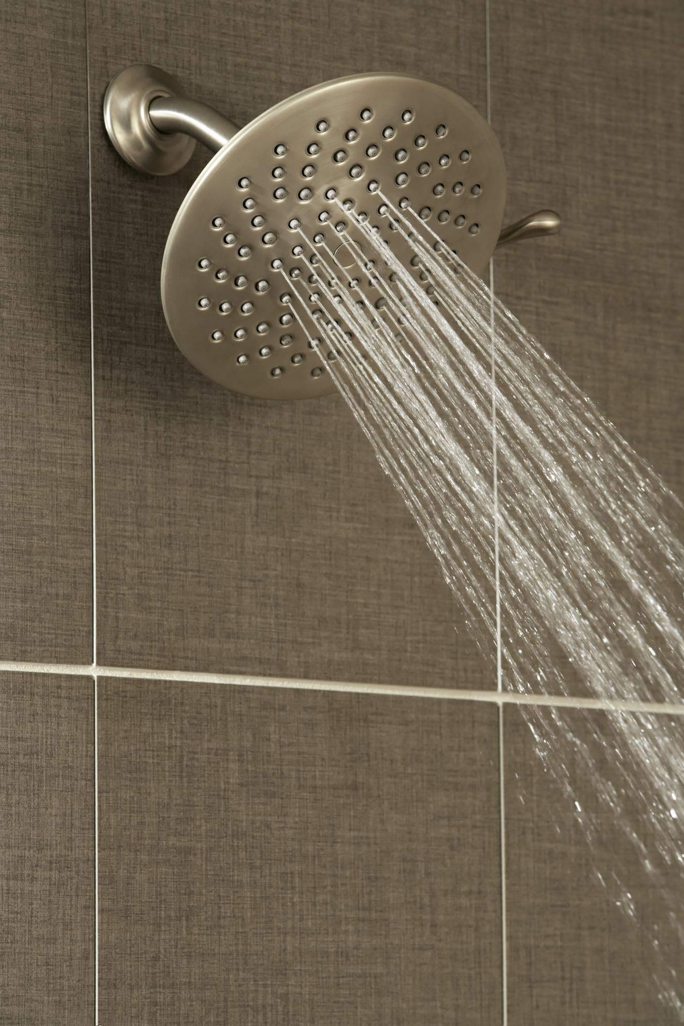 Brushed gold round showerhead with multiple spray holes mounted on wall arm, water streams flowing downward.