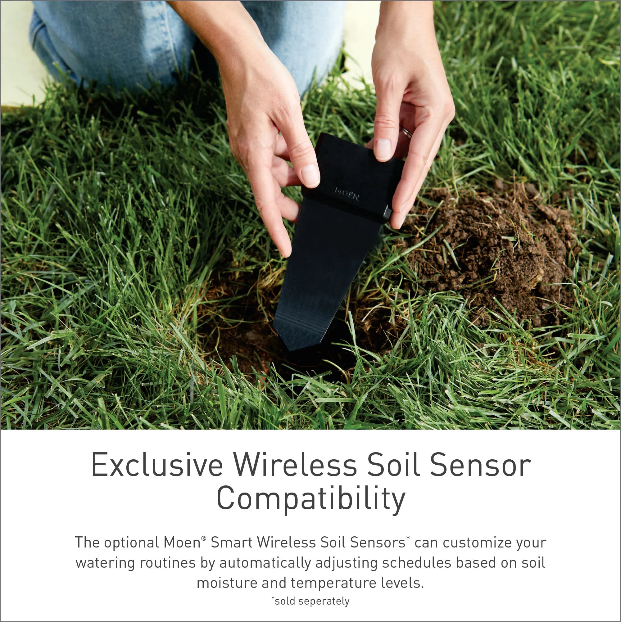 Person's hands holding black wireless soil sensor in ground next to grass.
