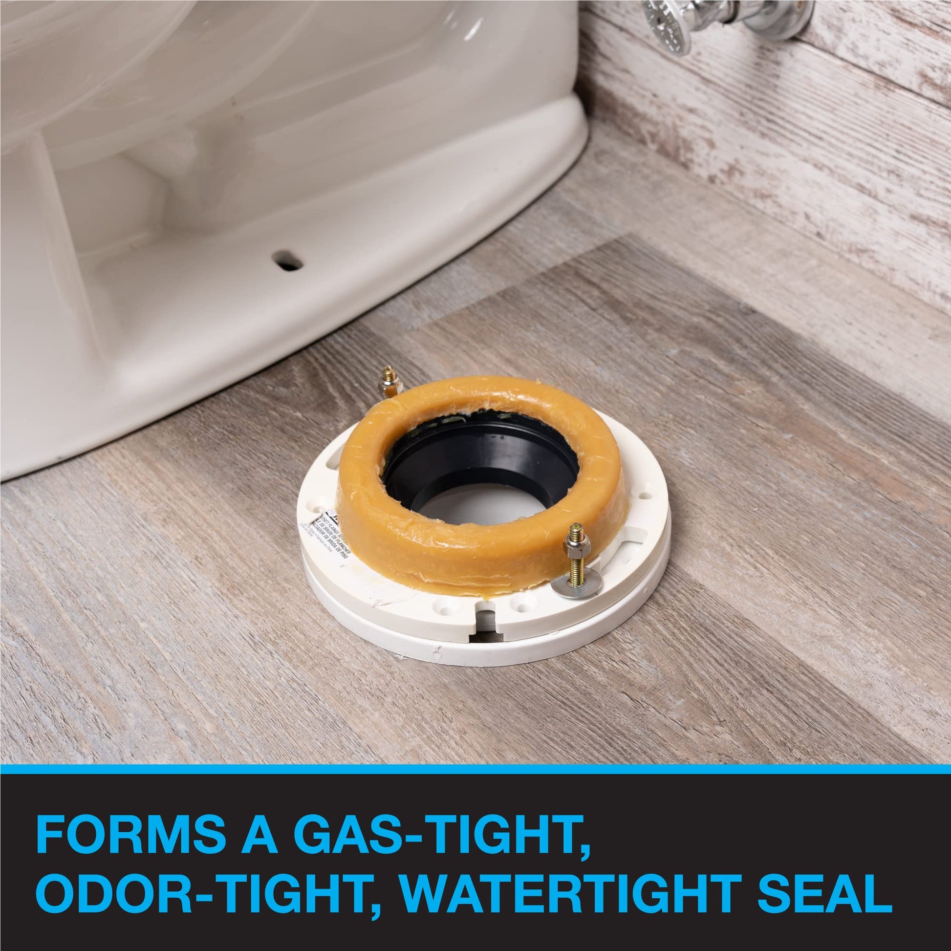 Toilet wax ring with white base, tan wax seal, black center, and brass bolts on wooden floor next to toilet.
