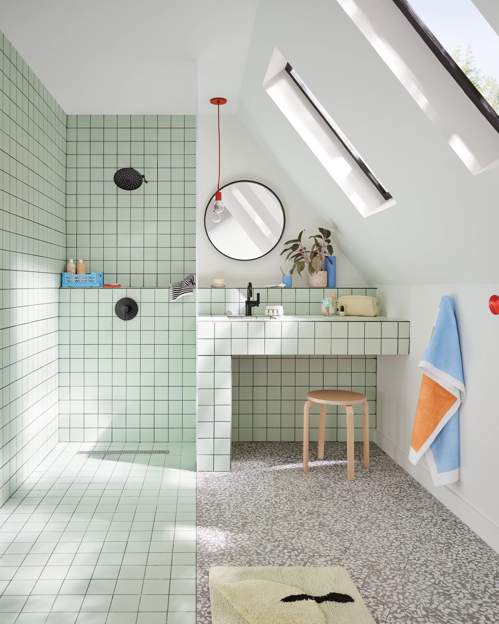 Matte black circular shower head mounted on wall above green tiled shower area.