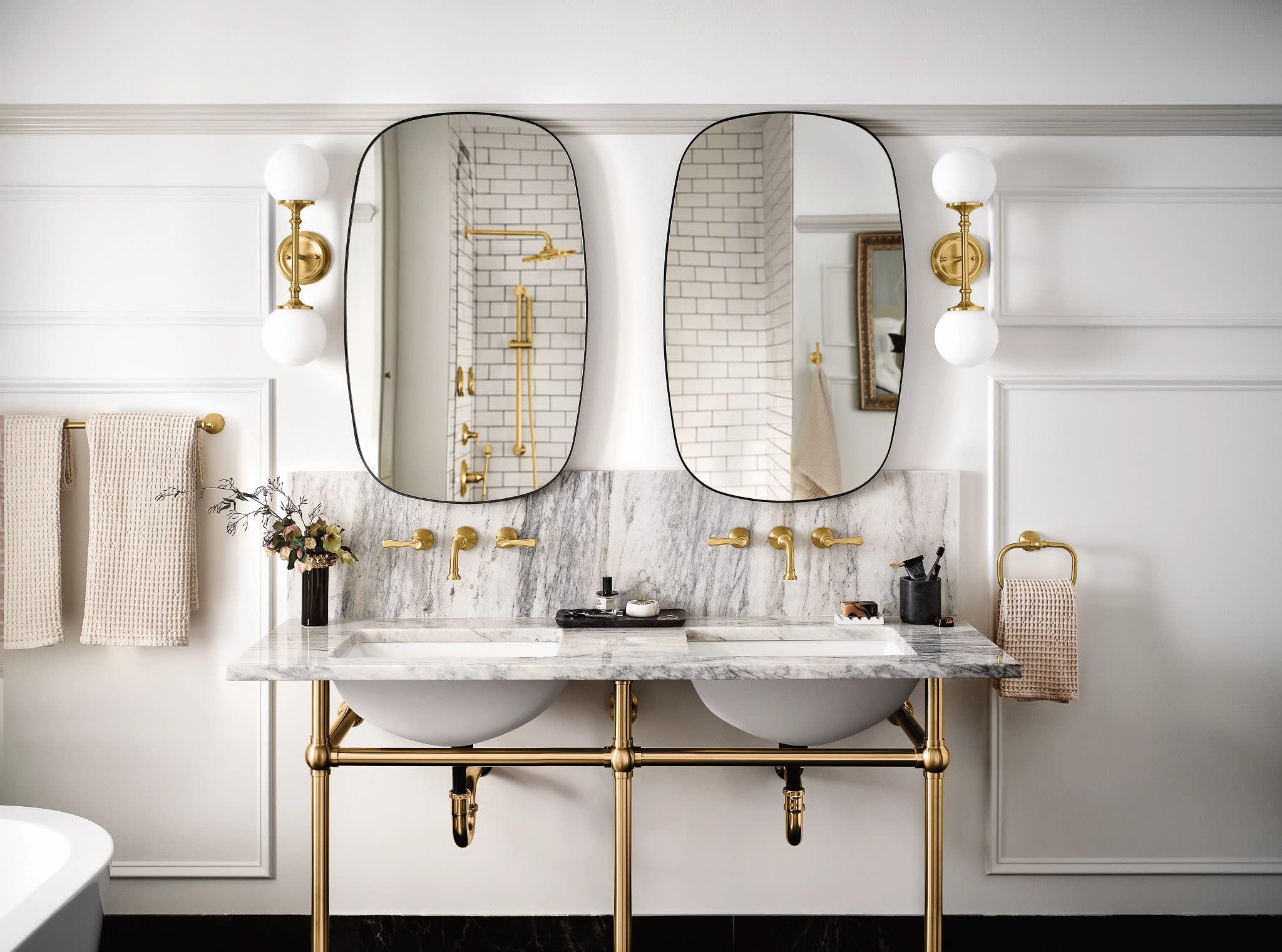 Brushed gold widespread bathroom faucet trim with traditional lever handles mounted on marble backsplash above dual sinks.