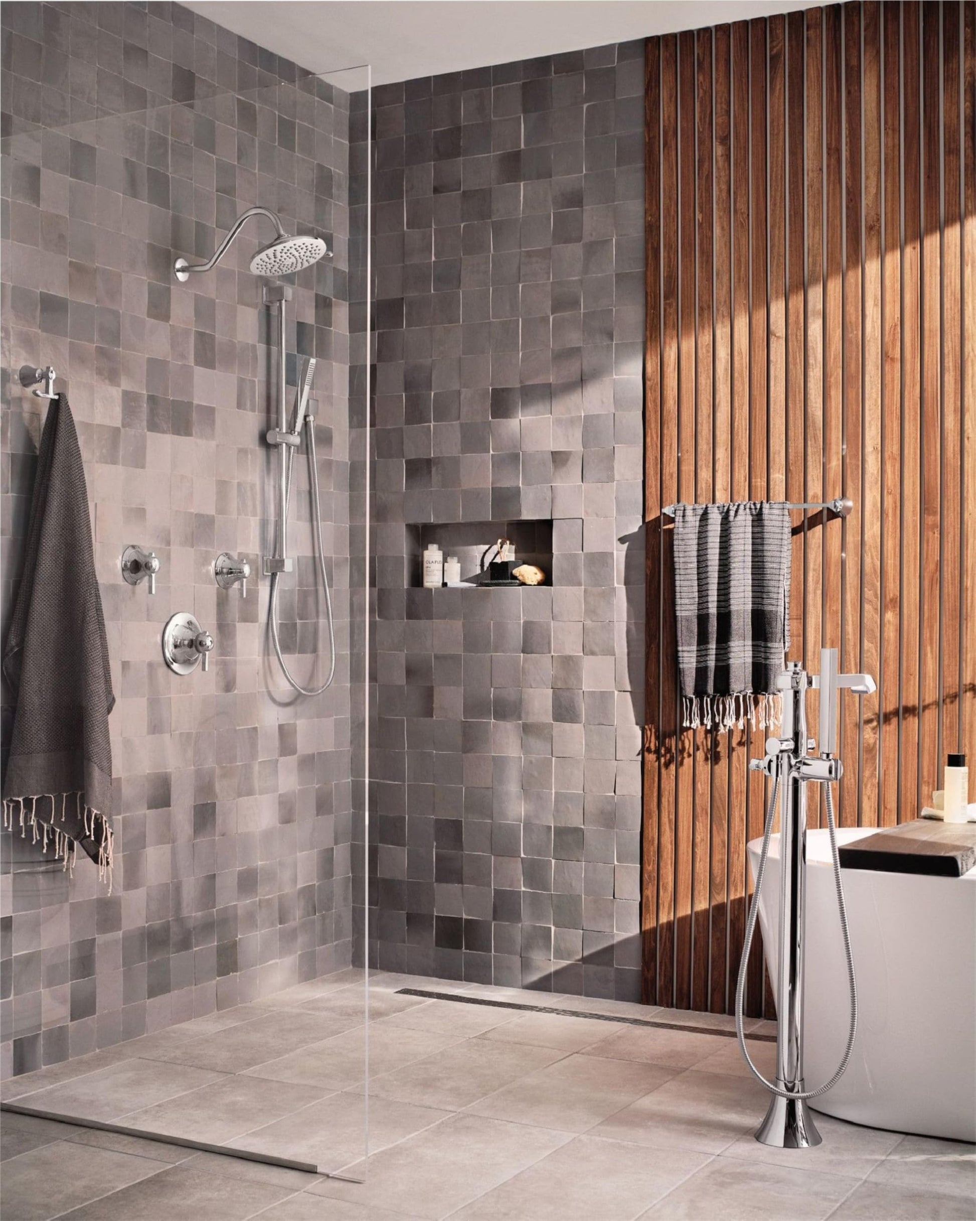 Chrome handheld showerhead with adjustable slide bar mounted on gray tile shower wall with hose and controls.