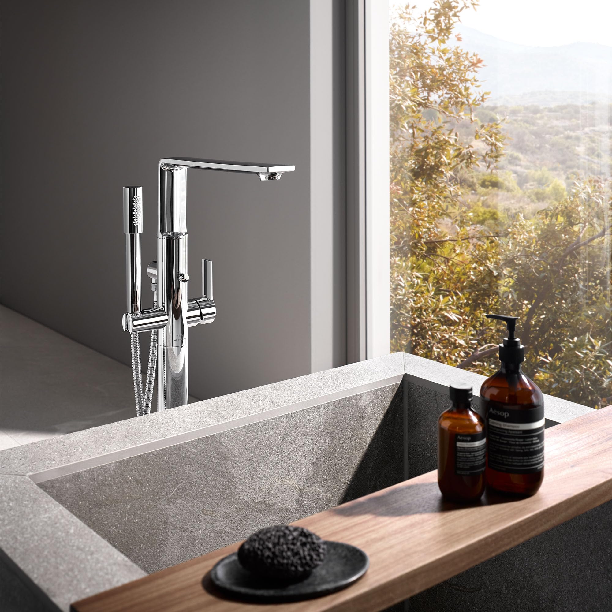 Chrome freestanding tub faucet with single handle and detached hand shower mounted on bathroom countertop.