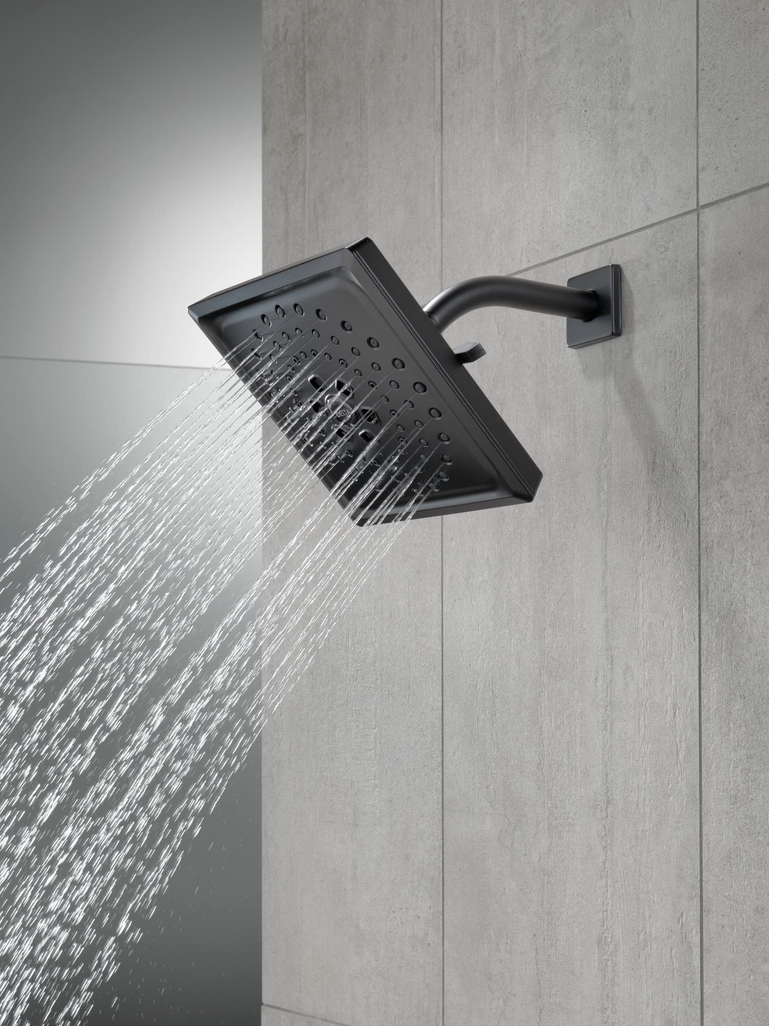Matte black square shower head with curved arm mounted on tile wall, dispensing water.