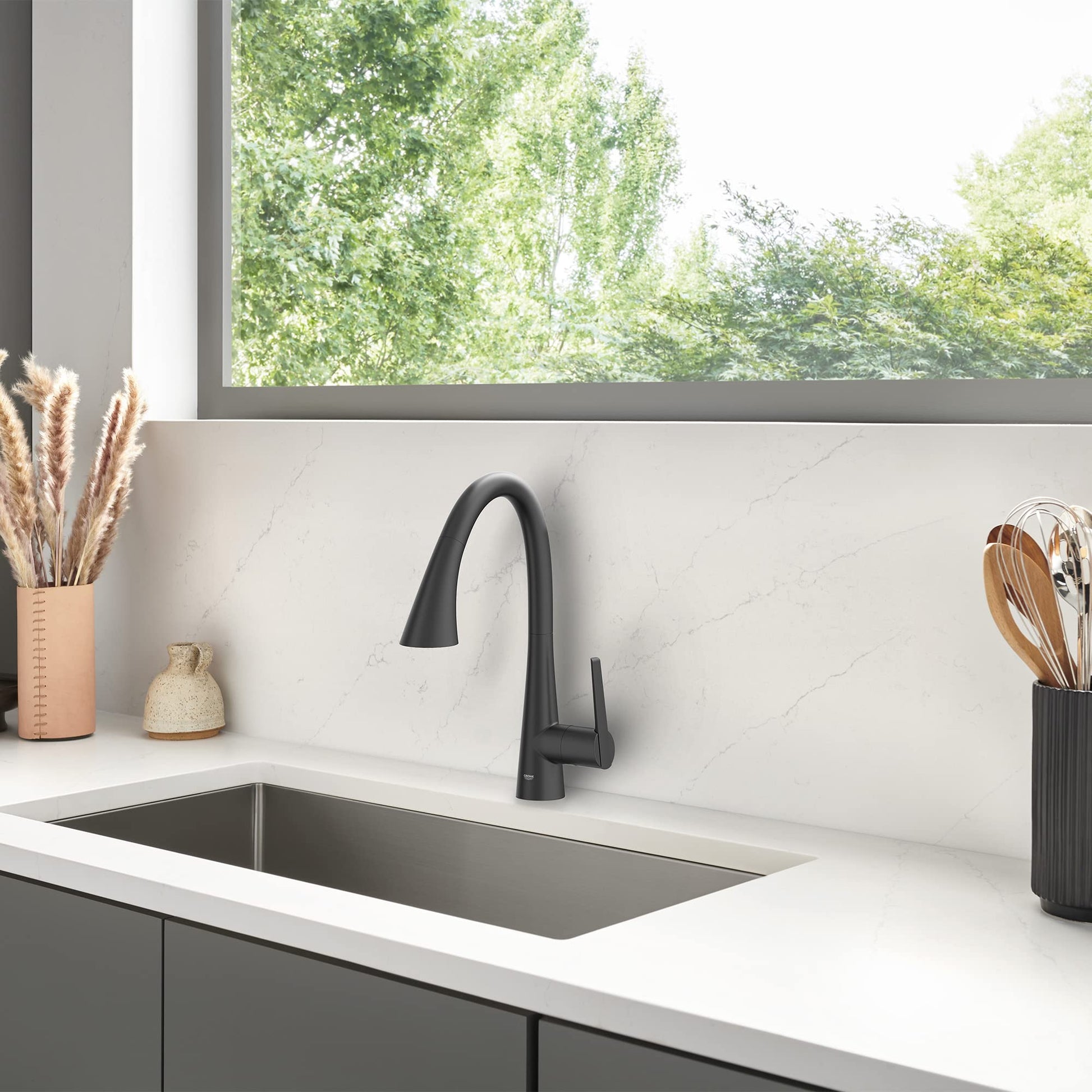 Matte black single-handle pull-down kitchen faucet with curved spout mounted above rectangular sink.