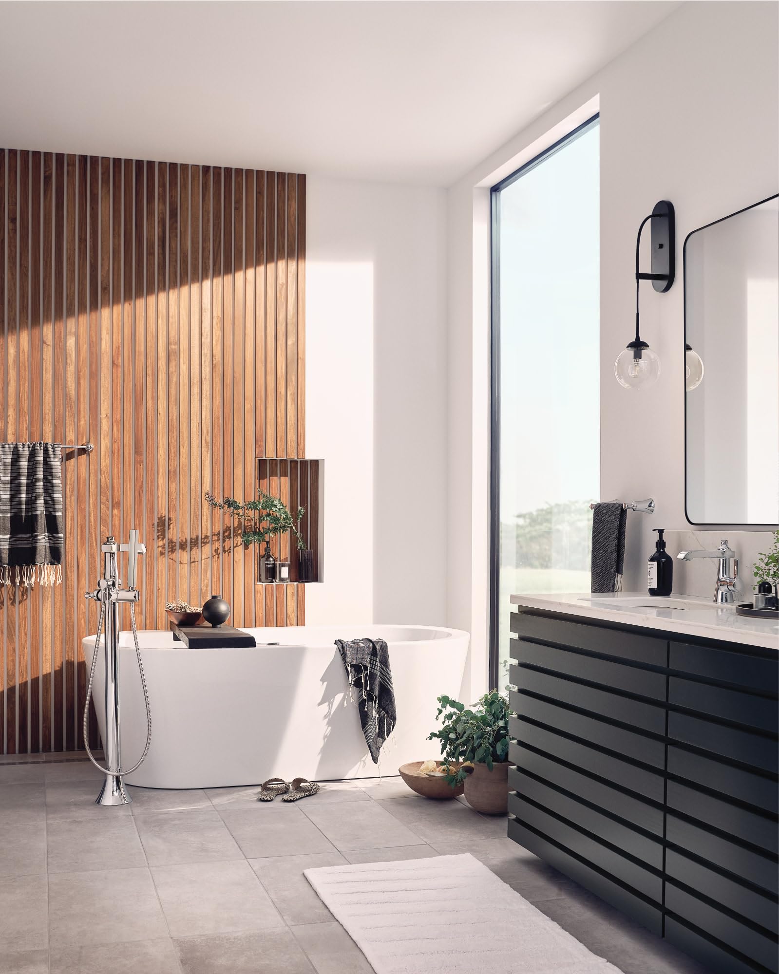 Polished nickel freestanding tub filler with single handle and handheld showerhead mounted on floor next to white soaking tub