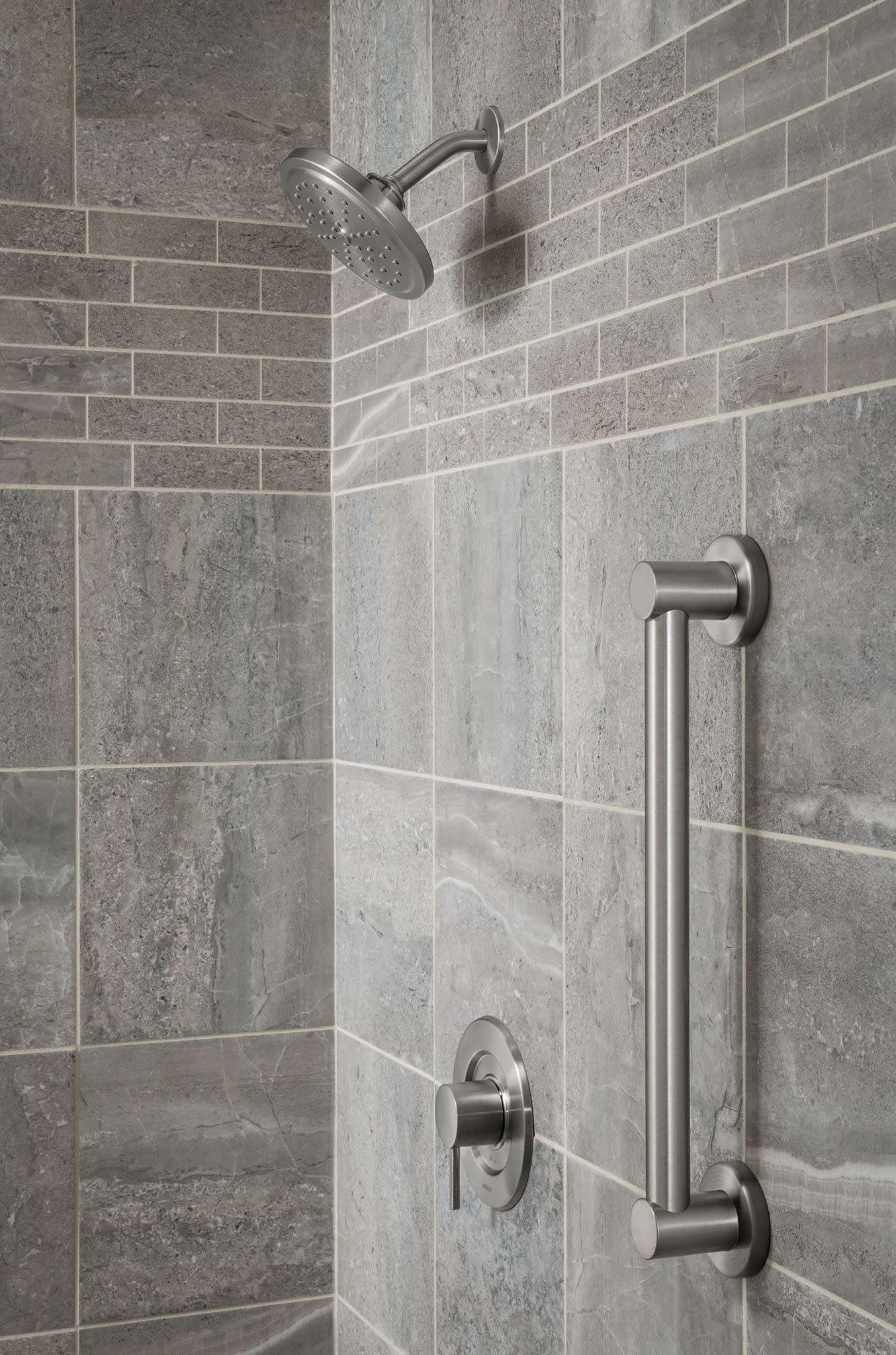 Brushed nickel stainless steel grab bar mounted vertically on tile shower wall next to showerhead and controls.