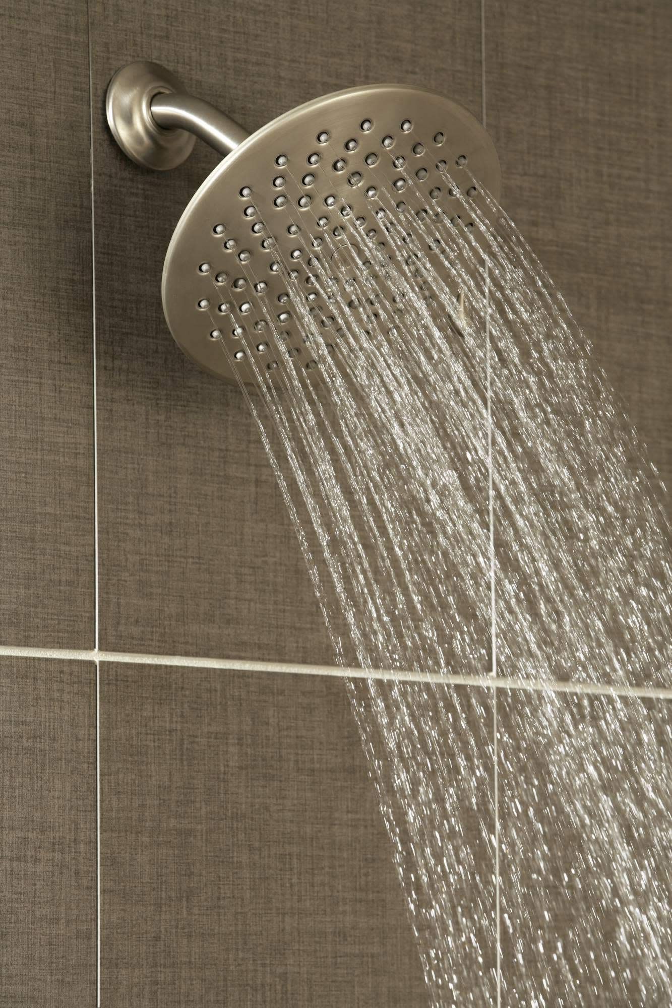 Brushed gold rainshower head mounted on wall with water streaming from multiple jets across circular face.