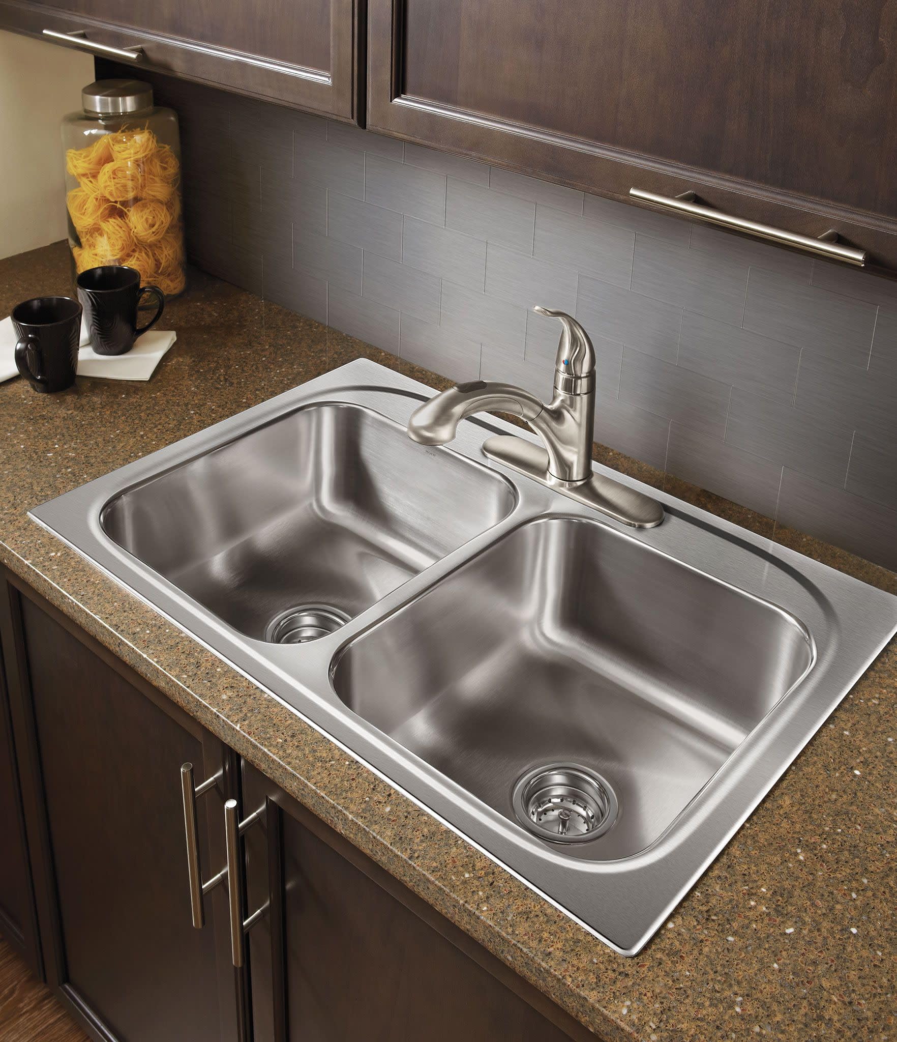 Chrome single-handle kitchen faucet with curved spout installed above stainless steel double-bowl sink.
