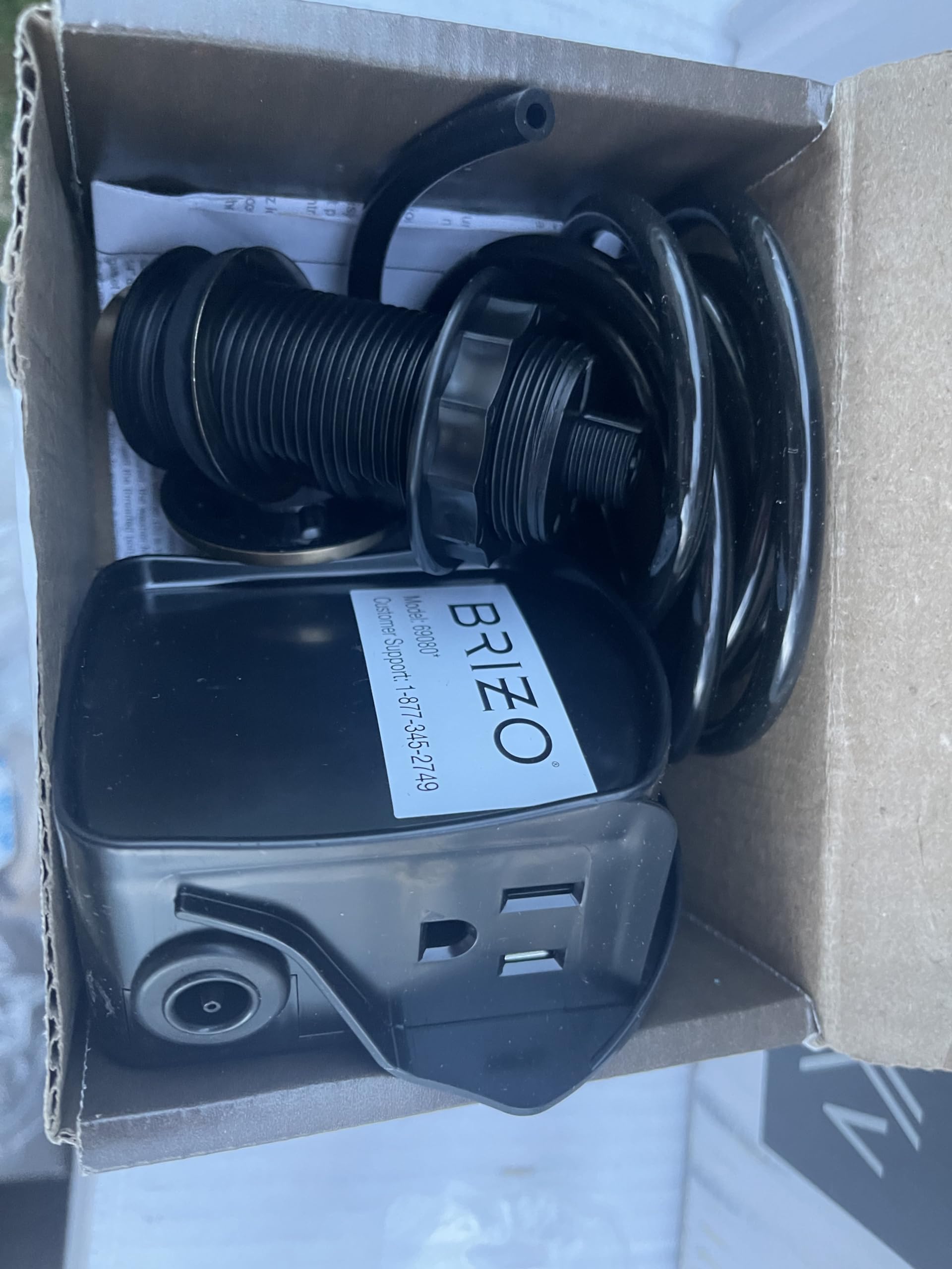 Brizo air switch with dual outlet, black plastic housing with coiled tubing and control unit in cardboard packaging.