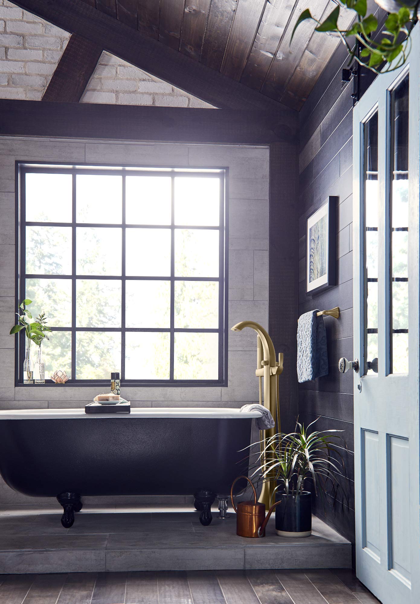 Brass floor-mount tub filler faucet installed next to a black clawfoot bathtub in a tiled bathroom.