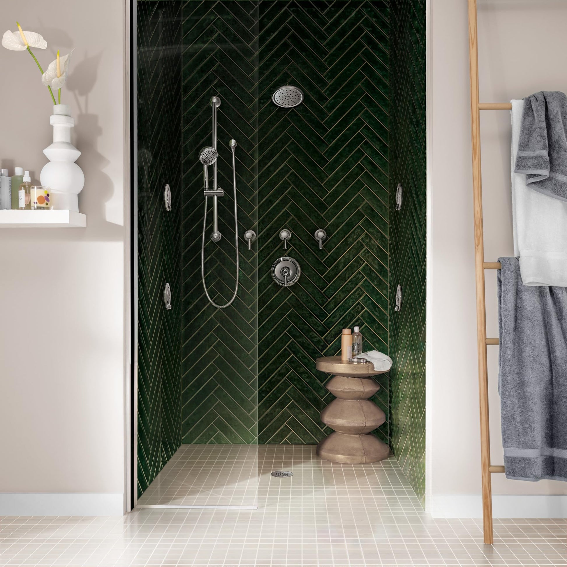Chrome rainshower showerhead mounted on wall above multiple body jets in modern shower enclosure with green herringbone tile.