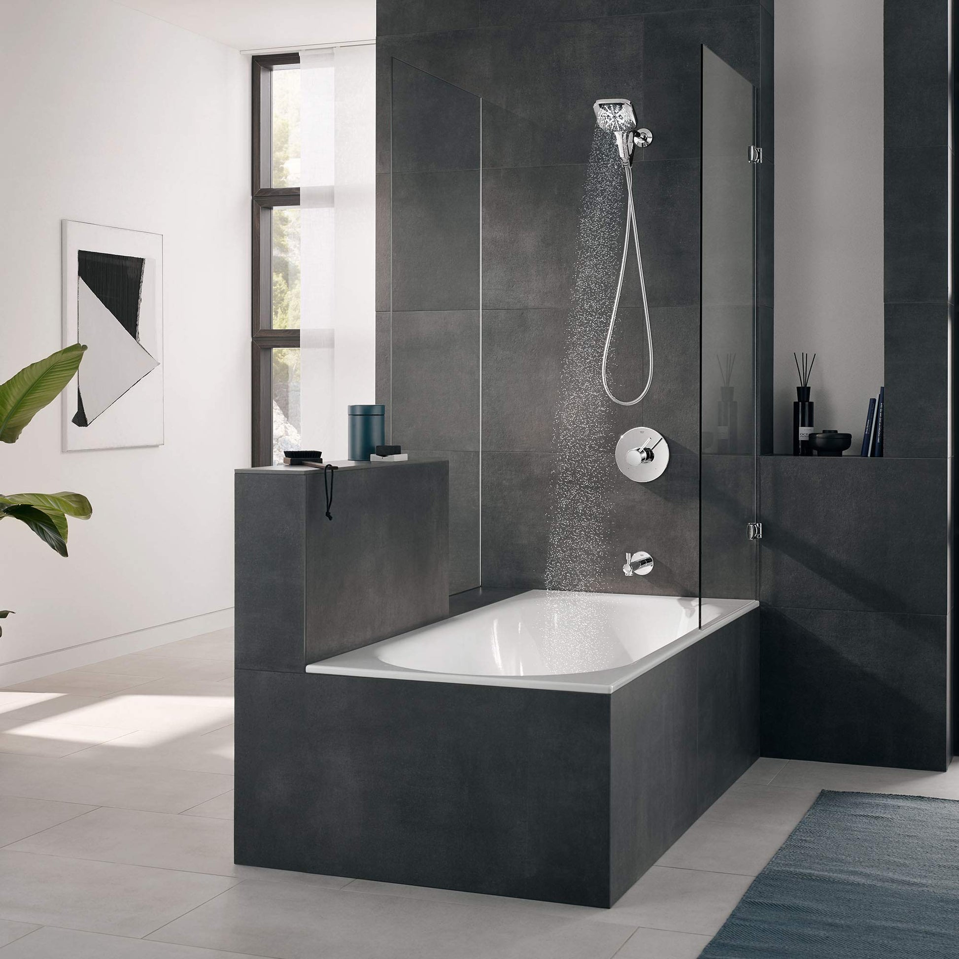 Chrome hand shower with flexible hose mounted on dark tile bathroom wall above bathtub.