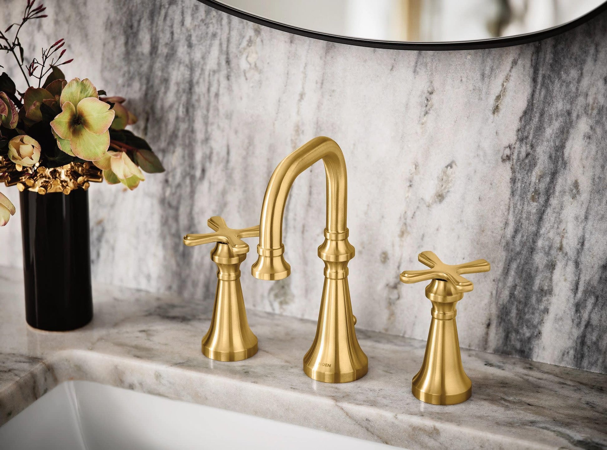 Brushed gold three-piece bathroom faucet with curved spout and cross handles mounted on marble countertop.