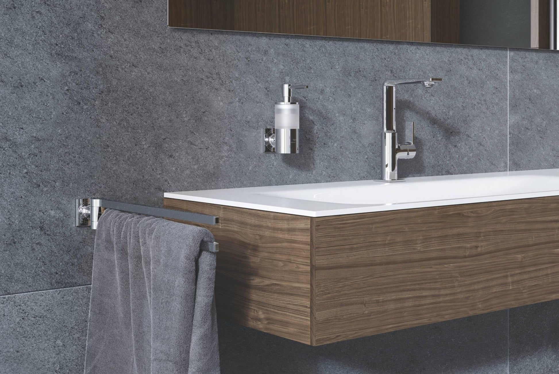 Chrome soap dispenser with pump mounted on gray tile bathroom wall above wooden vanity.