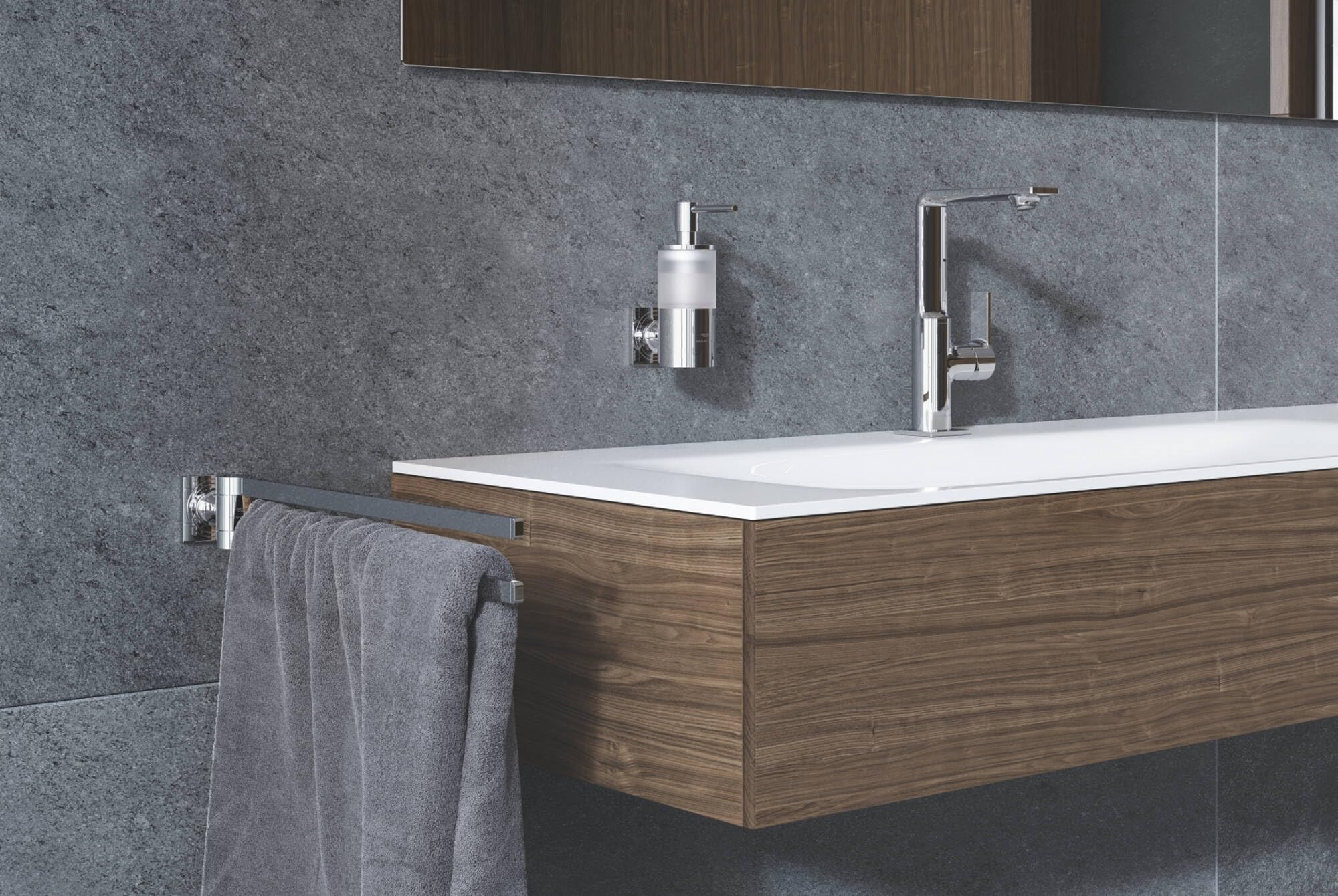 Chrome soap dispenser with pump mounted on gray tile bathroom wall above wooden vanity.
