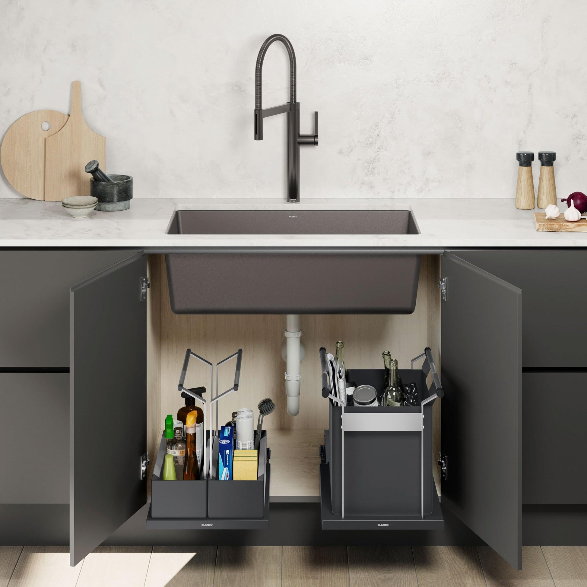 Black double storage caddy with compartments positioned under kitchen sink, holding cleaning supplies and utensils.