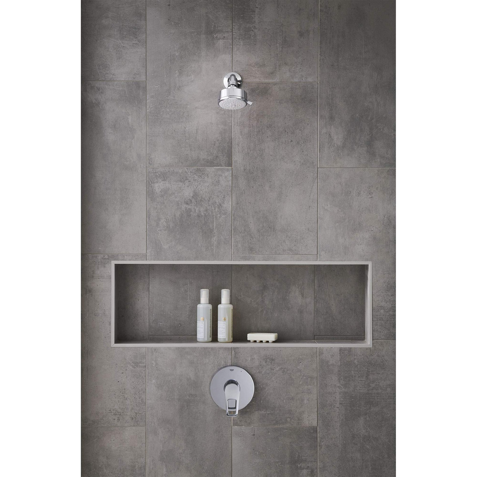 Chrome pressure balance valve trim with round escutcheon plate mounted on gray tile bathroom wall below overhead showerhead.